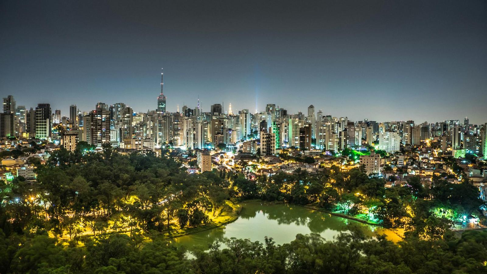 Night view of São Paulo's illuminated skyline with a park and lake in the foreground