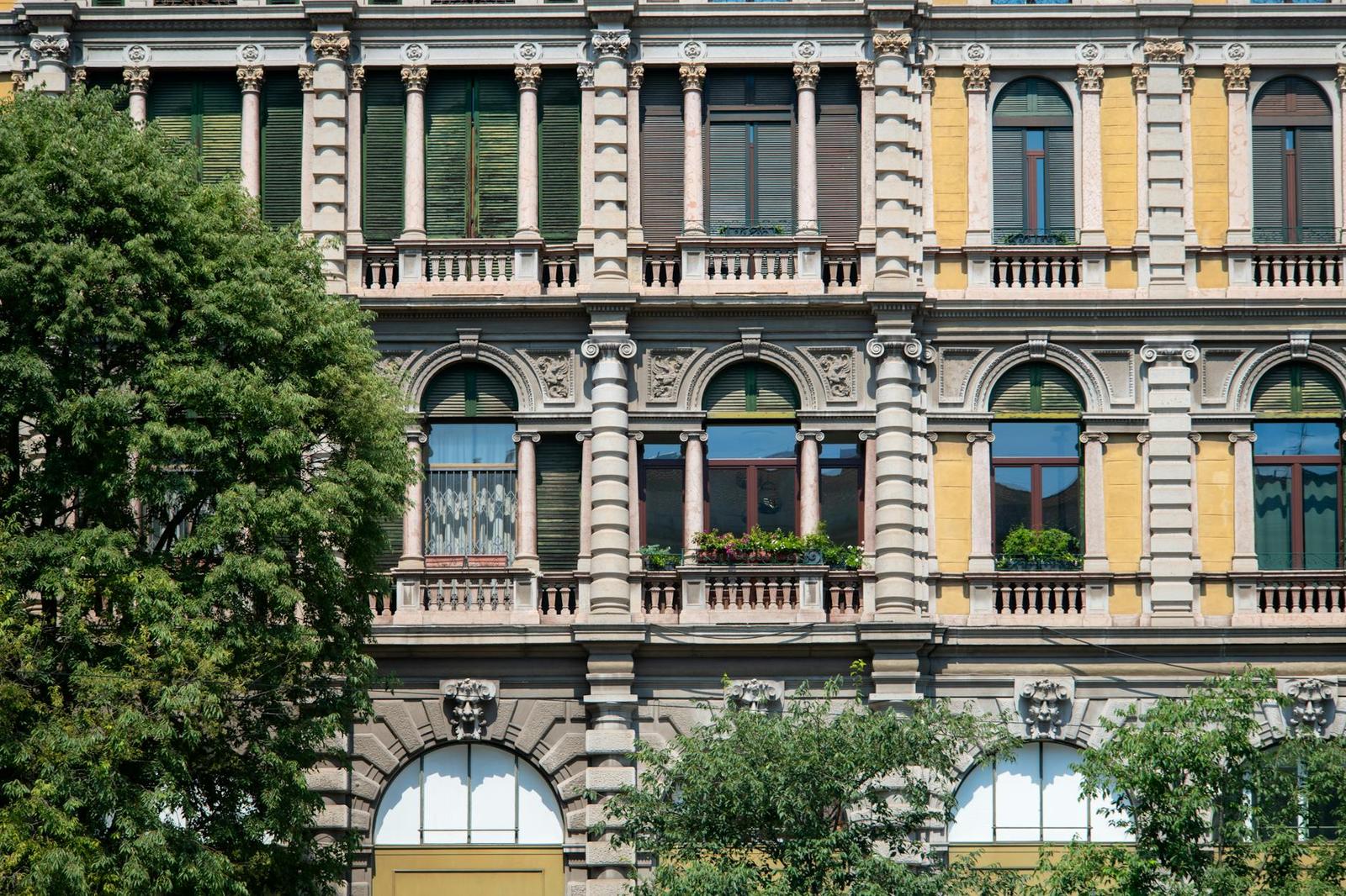 An ornate multi-storey facade with arched balconies and flower boxes behind a tree