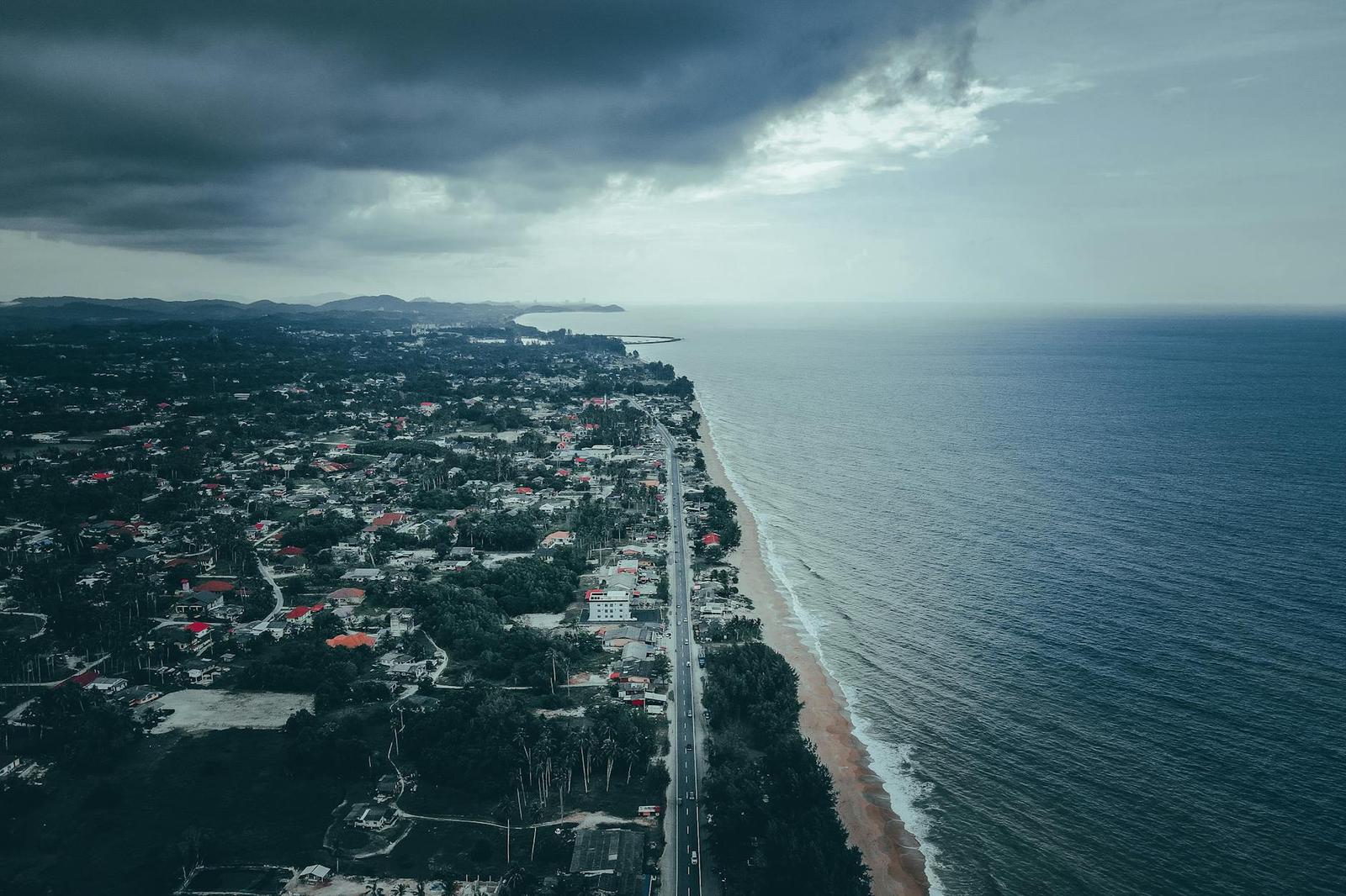 Aerial view of a coastal town road running along the shoreline under storm clouds