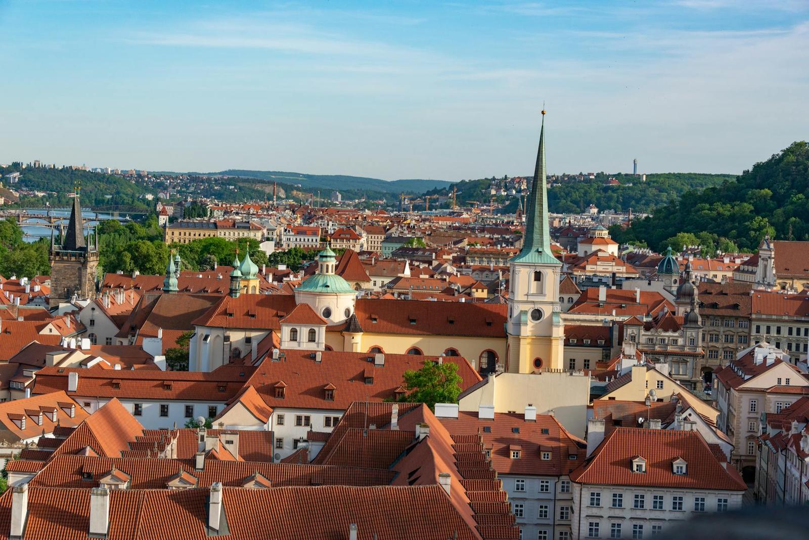Aerial view of Prague showcasing red rooftops and historic landmarks under a clear blue sky