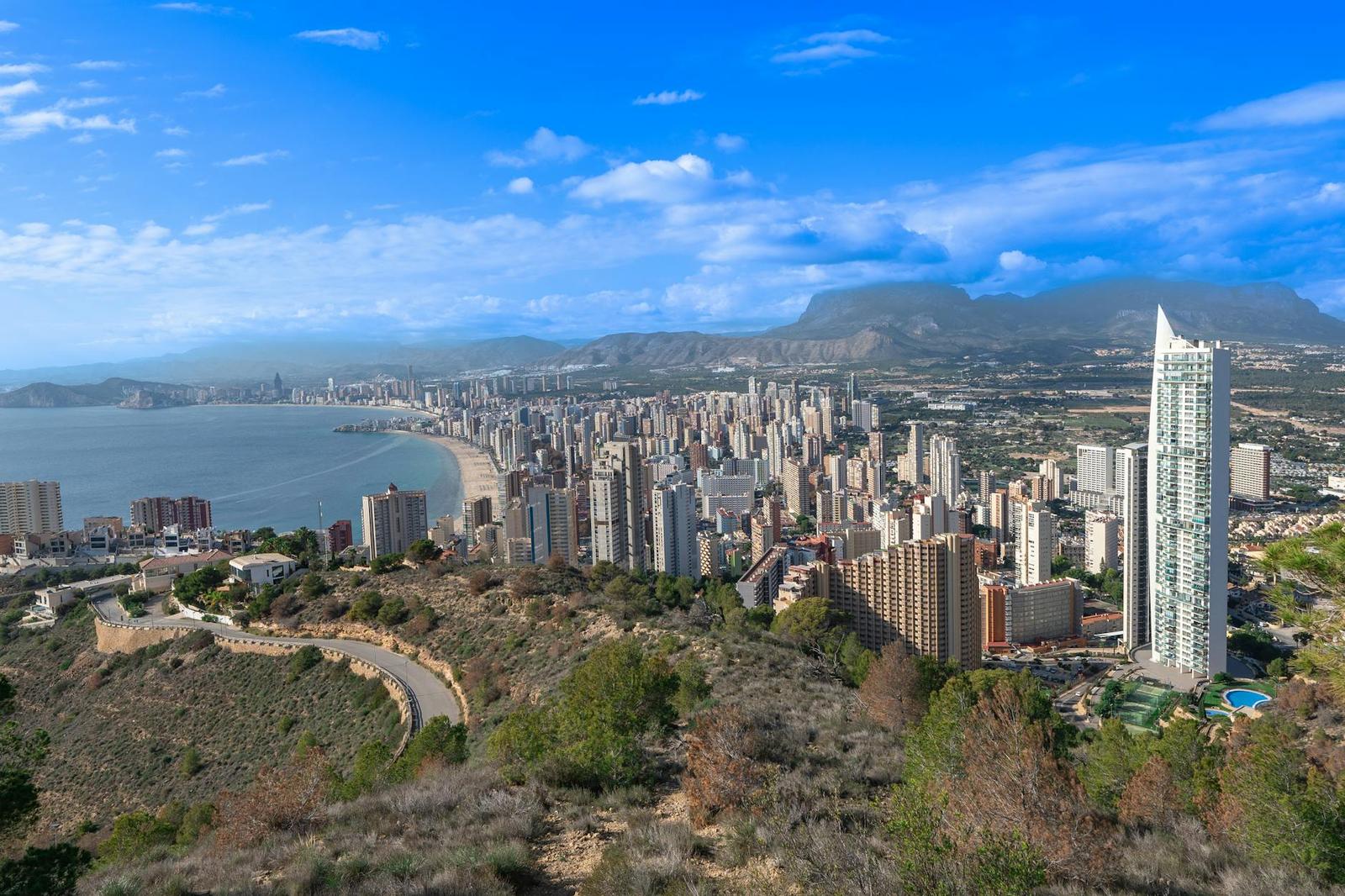 Aerial view of a high-rise beach city backed by mountains and a curving bay