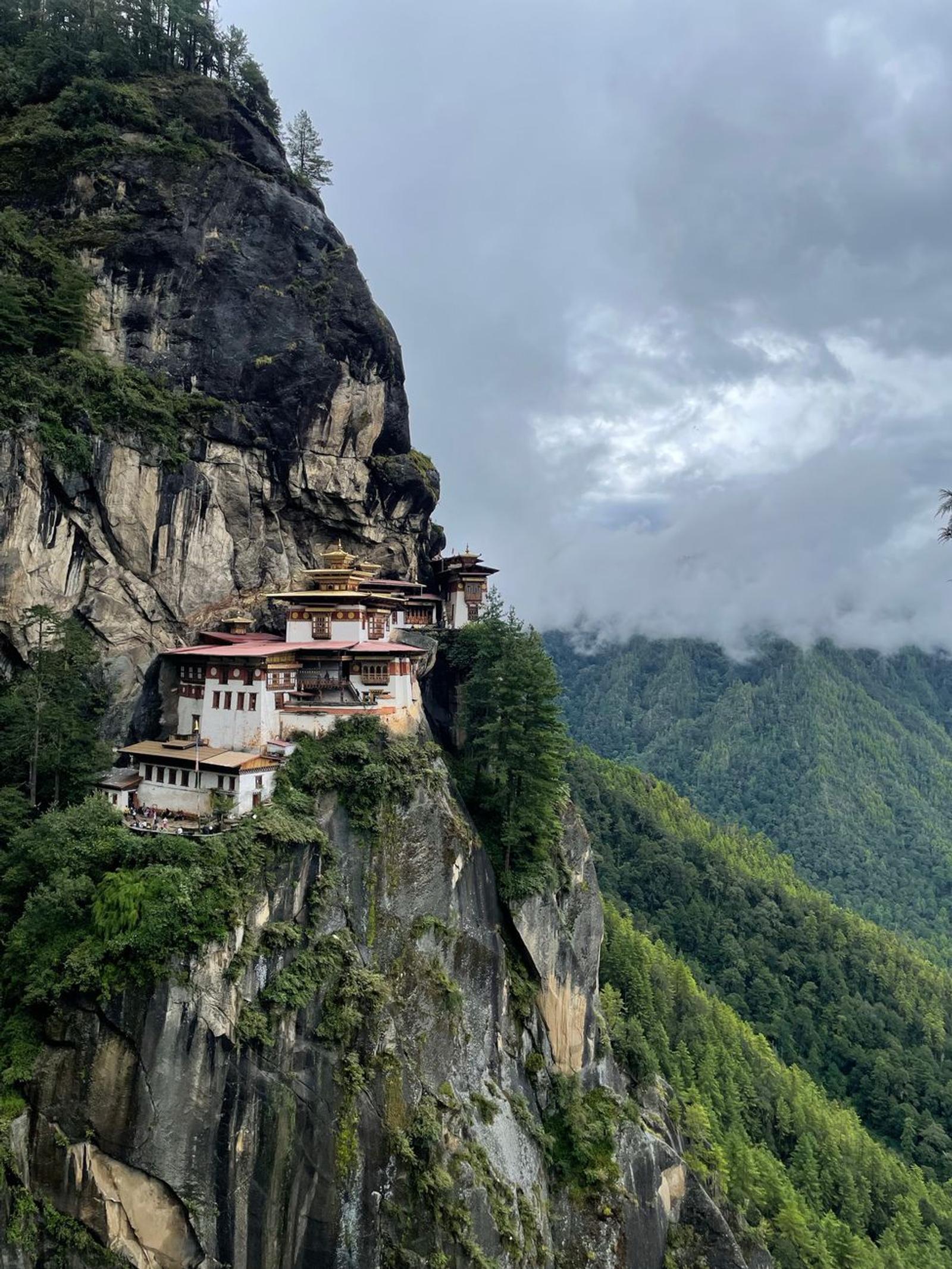 Taktsang Monastery perched on a cliff in Bhutan, surrounded by lush forest and clouds