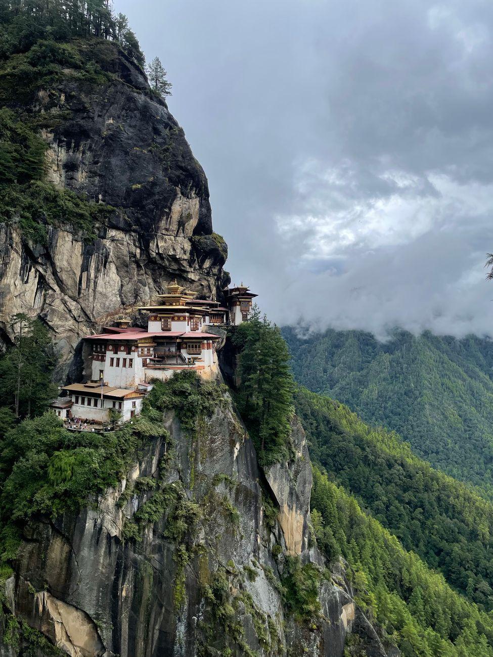 Taktsang Monastery perched on a cliff in Bhutan, surrounded by lush forest and clouds
