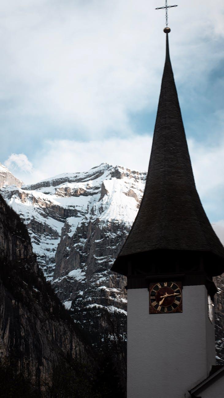 A church steeple stands against a majestic snowy mountain