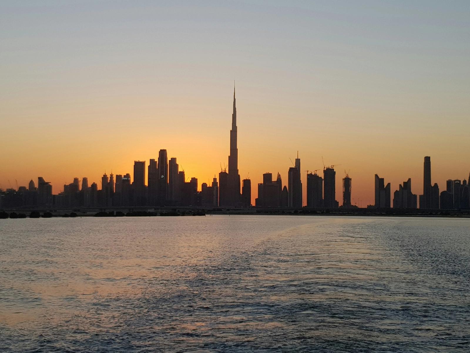 Burj Khalifa silhouetted above the Dubai skyline at sunset over water