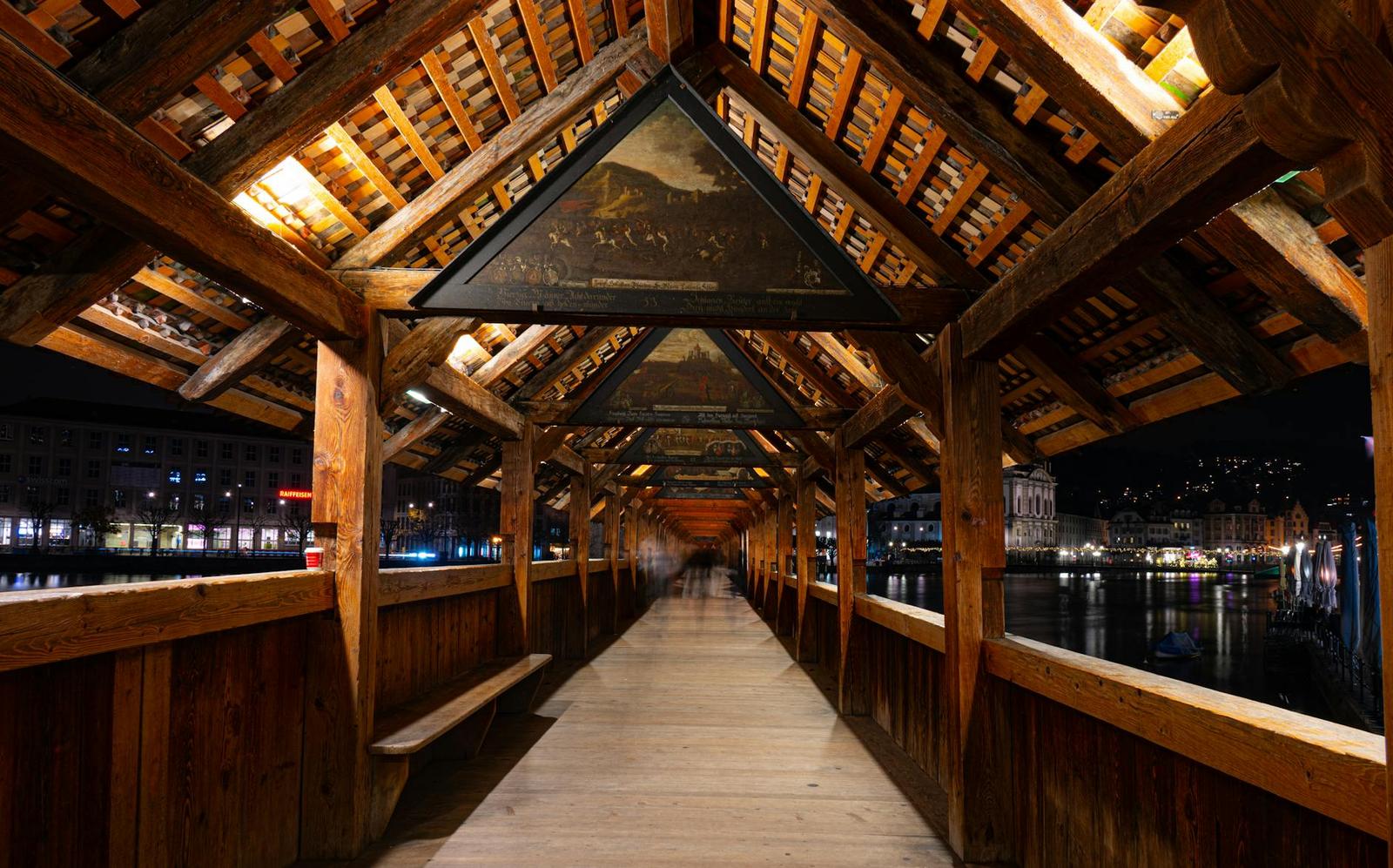 Inside a covered wooden bridge lined with painted historical panels along its beams