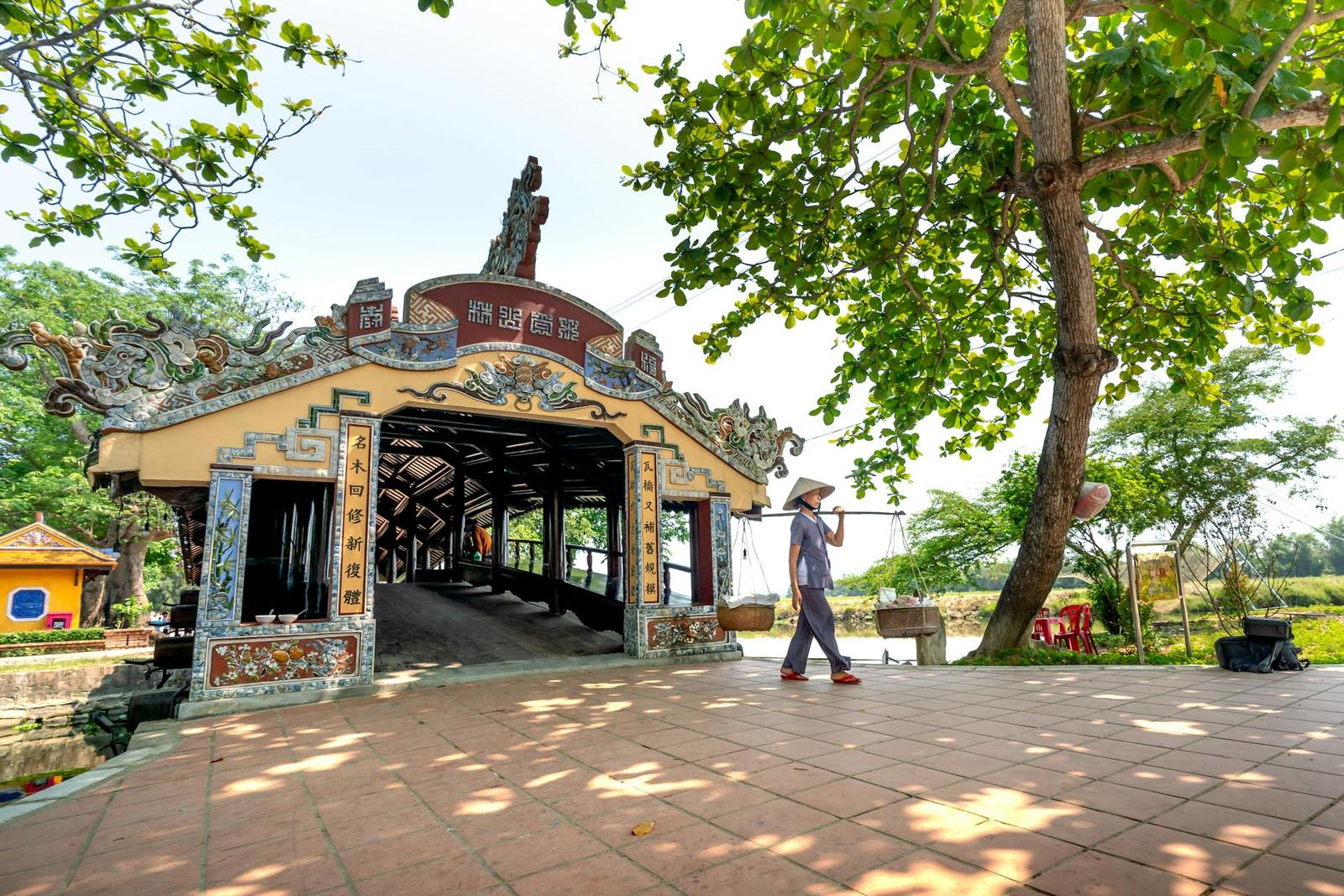 Person in a conical hat walking past a carved covered bridge