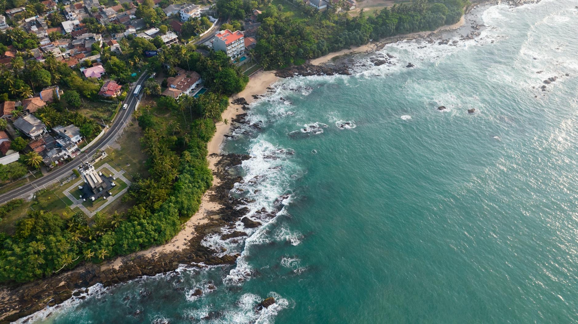 Aerial view of a rocky shoreline where turquoise waves meet a coastal village