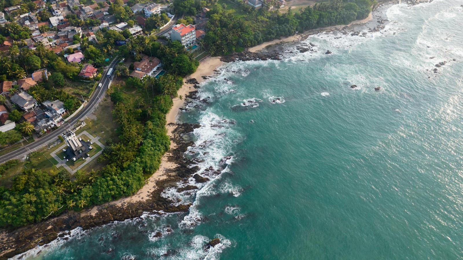 Aerial view of a rocky shoreline where turquoise waves meet a coastal village