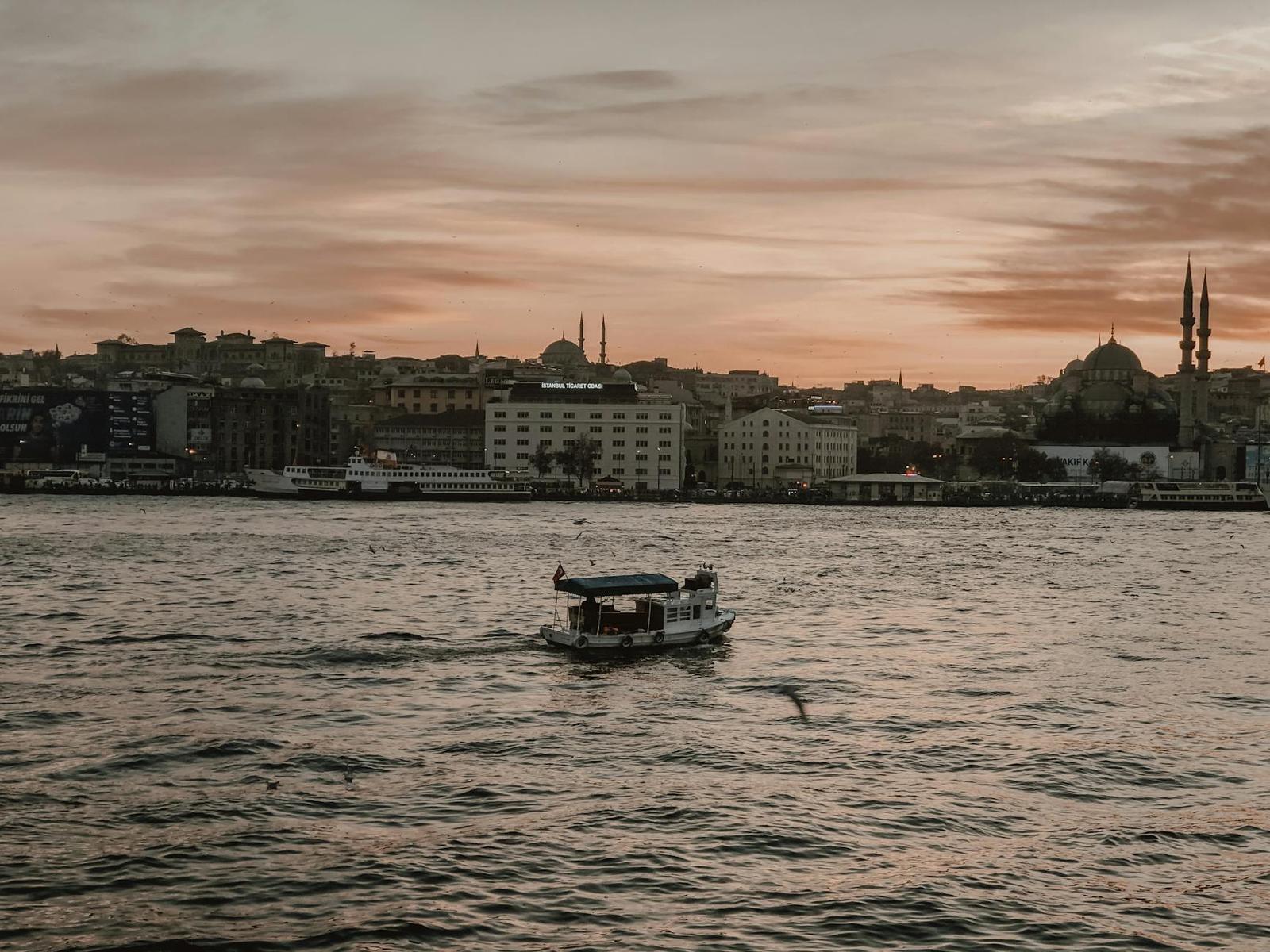 Small boat crossing calm water with a mosque skyline glowing at sunset