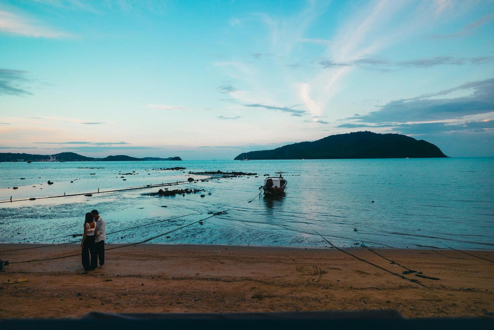 Couple standing on a beach at dusk with a moored boat offshore