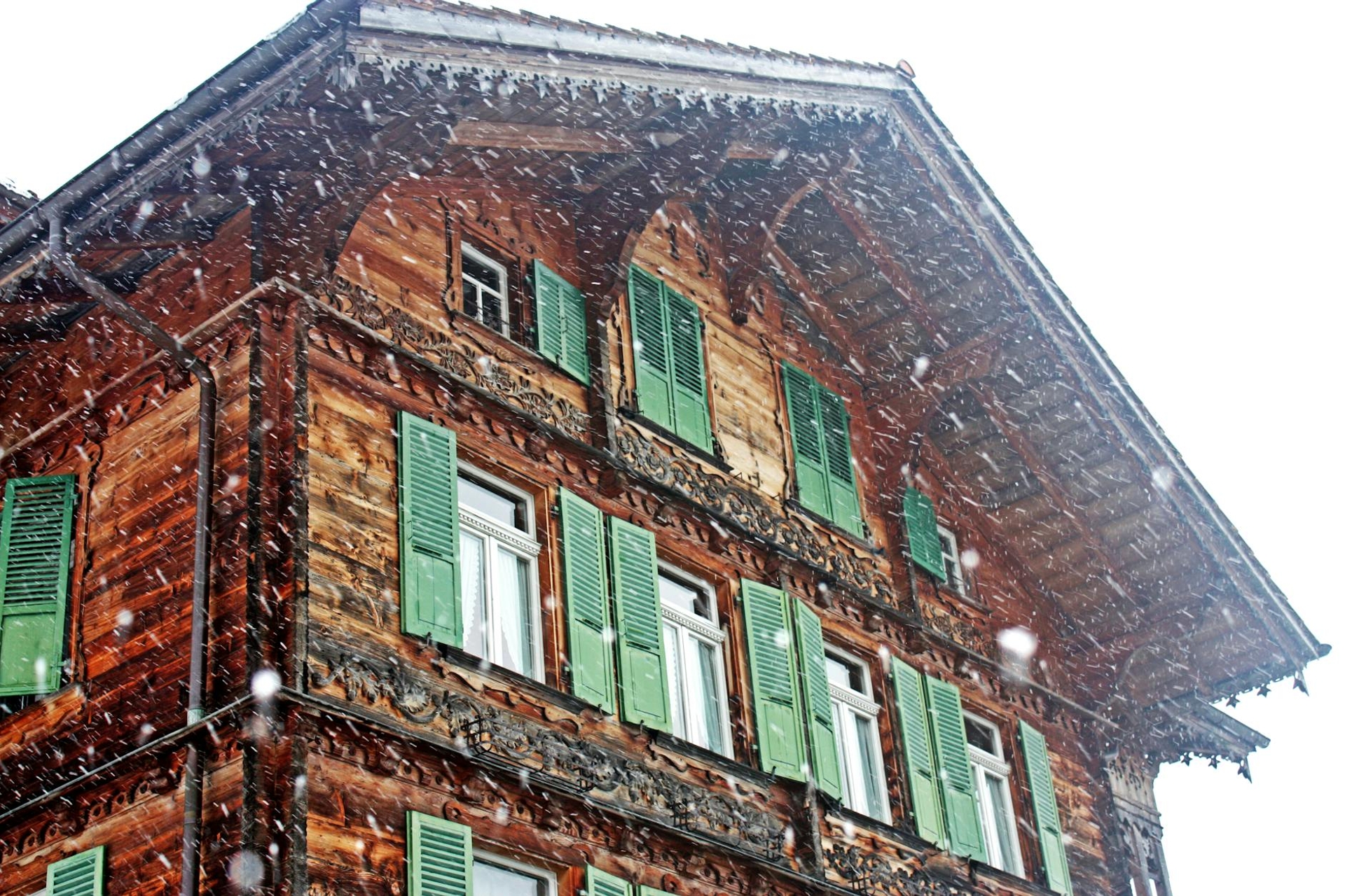 Snow falling on a carved wooden chalet facade with green shutters
