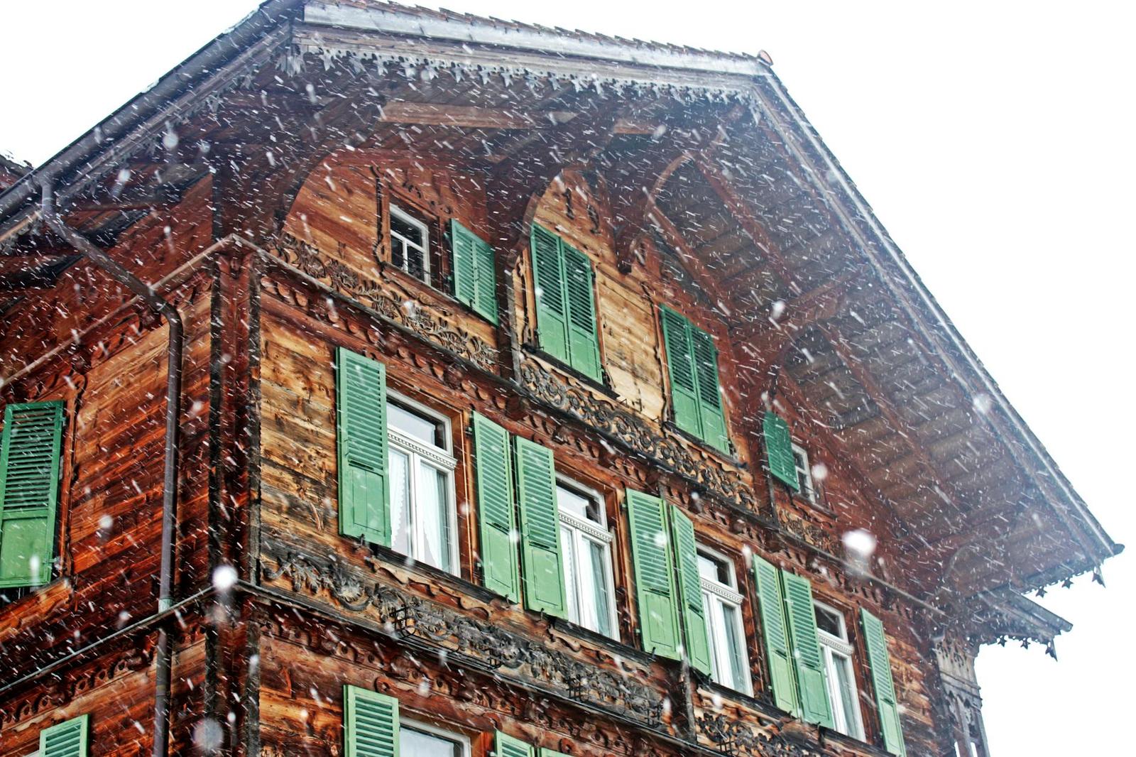Snow falling on a carved wooden chalet facade with green shutters
