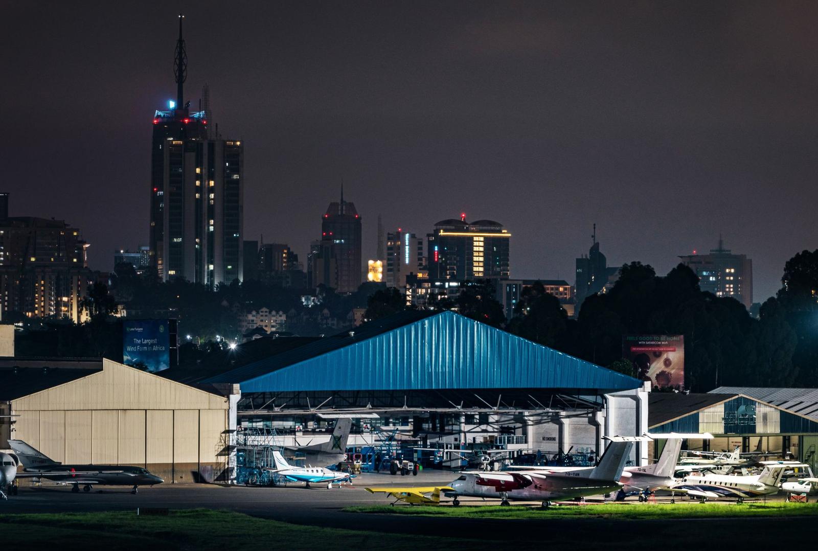 Private aircraft parked at a hangar with a lit city skyline behind at night