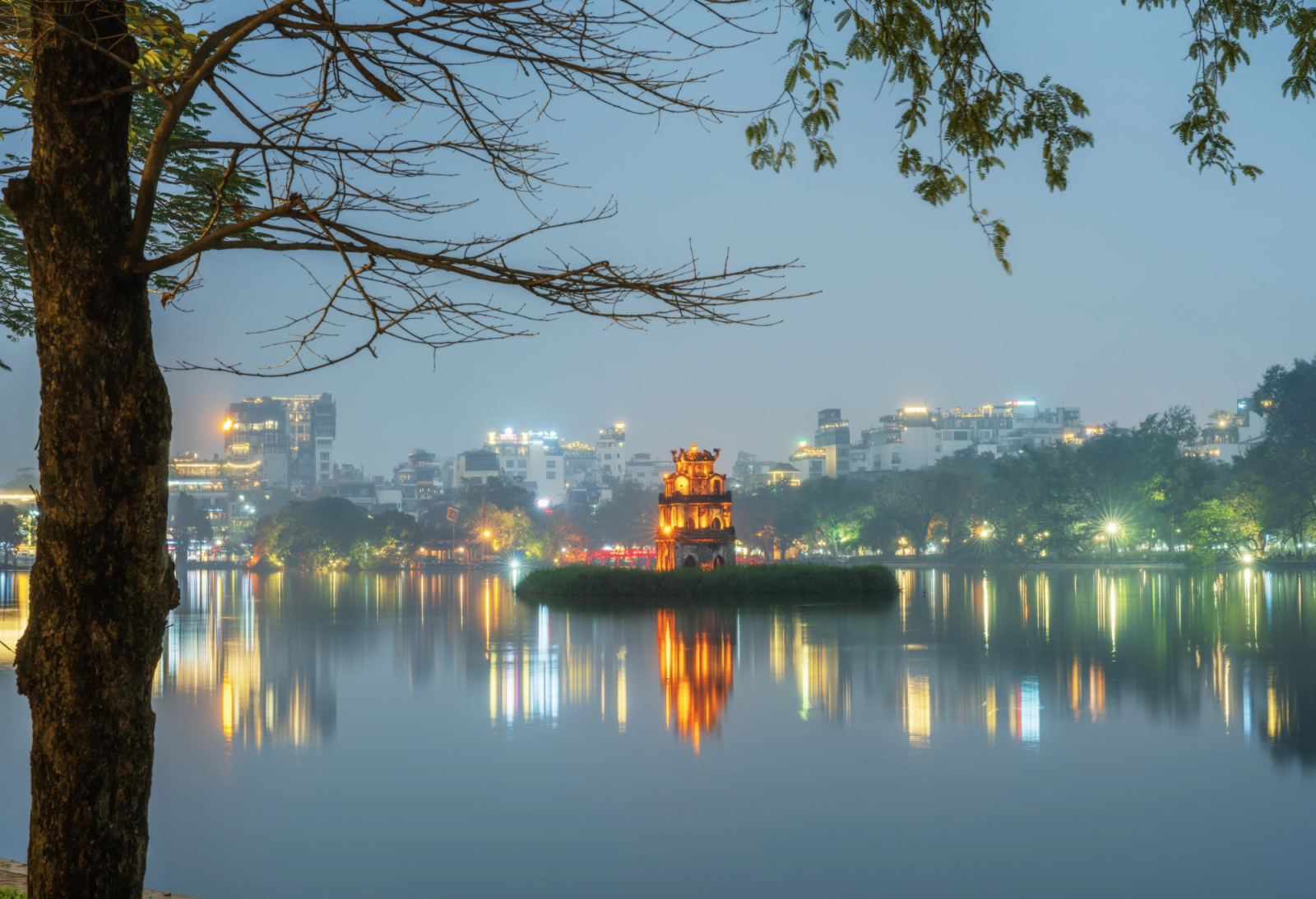 Calm evening scene of Hoan Kiem Lake reflecting city lights with Turtle Tower in Hanoi, Vietnam