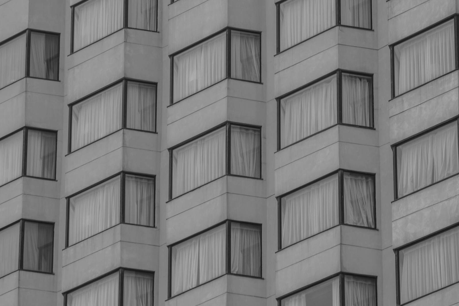 A black and white grid of angled high-rise windows with drawn curtains