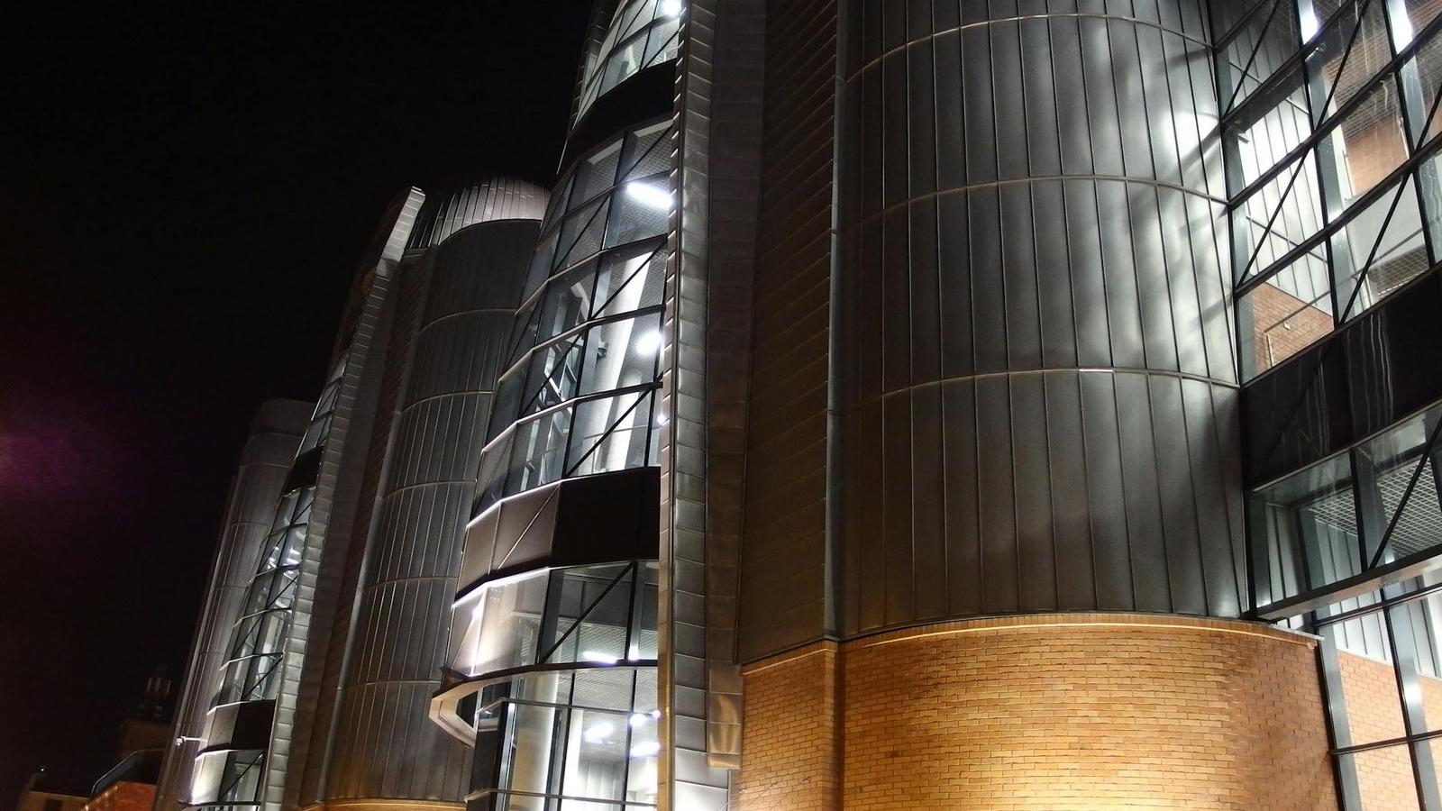 Angular glass and metal building facade lit up against a dark night sky