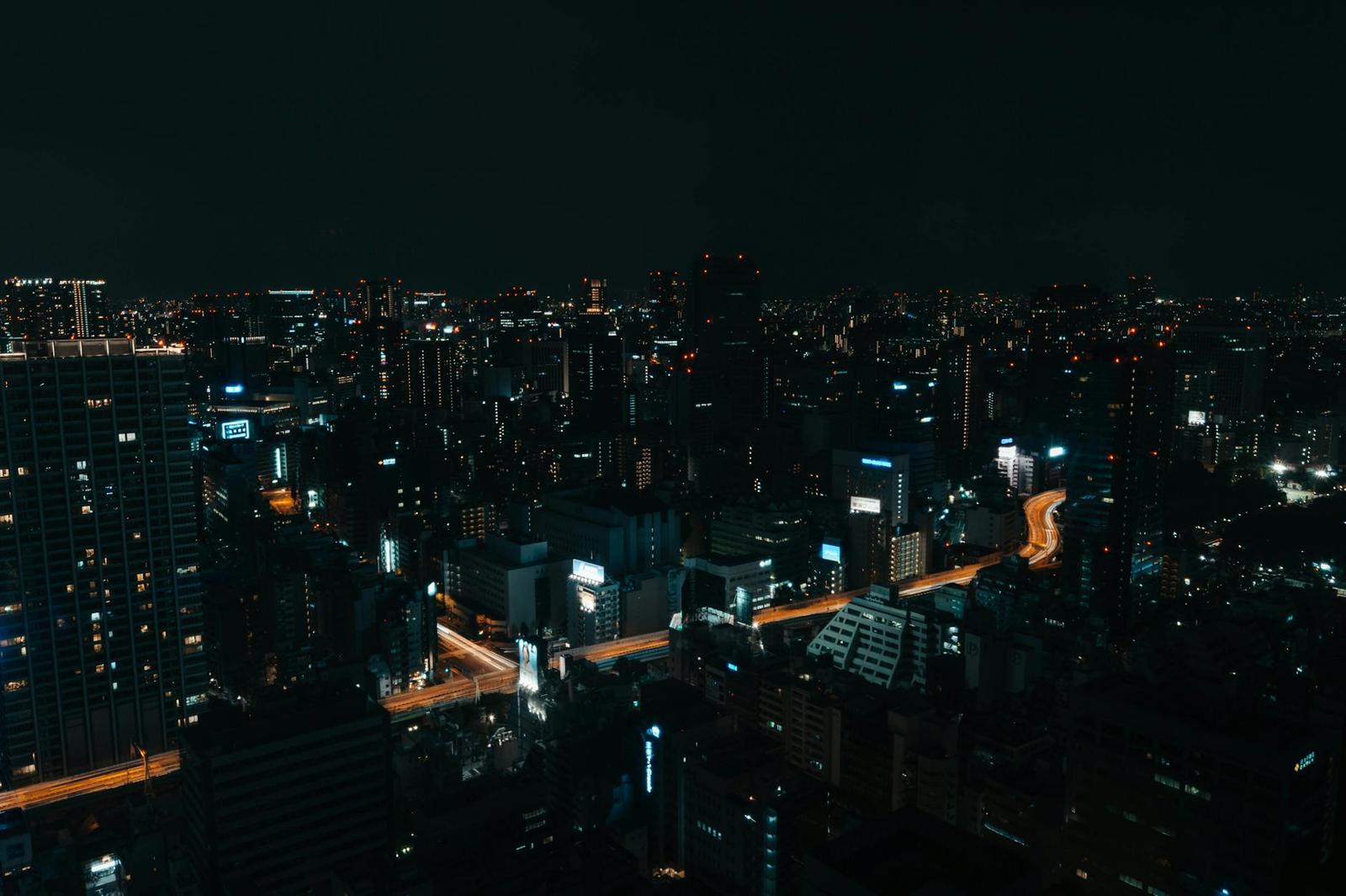 A dark aerial view of a city at night with a lit expressway curving through