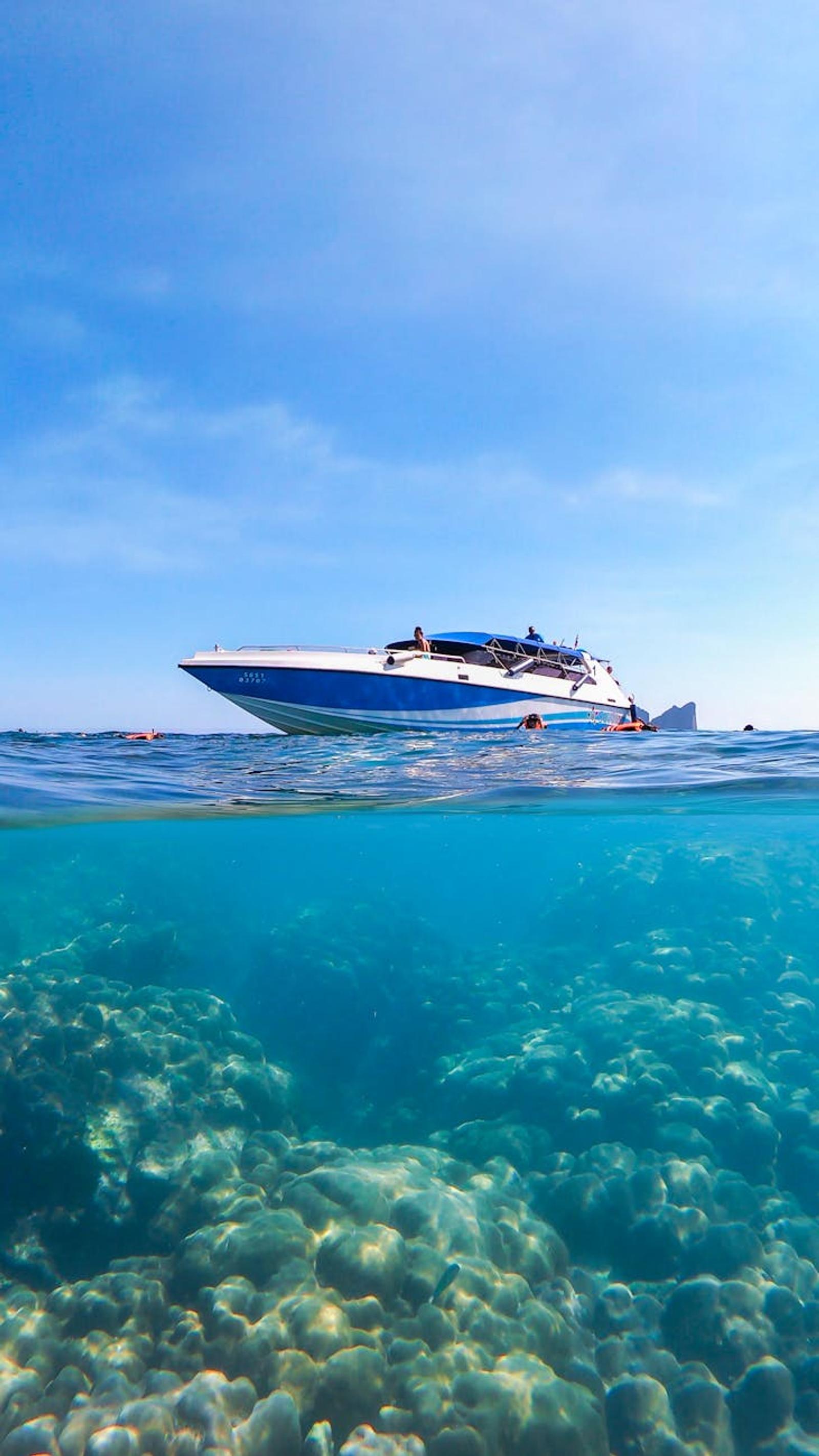 Speedboat anchored above a coral reef with swimmers in clear water