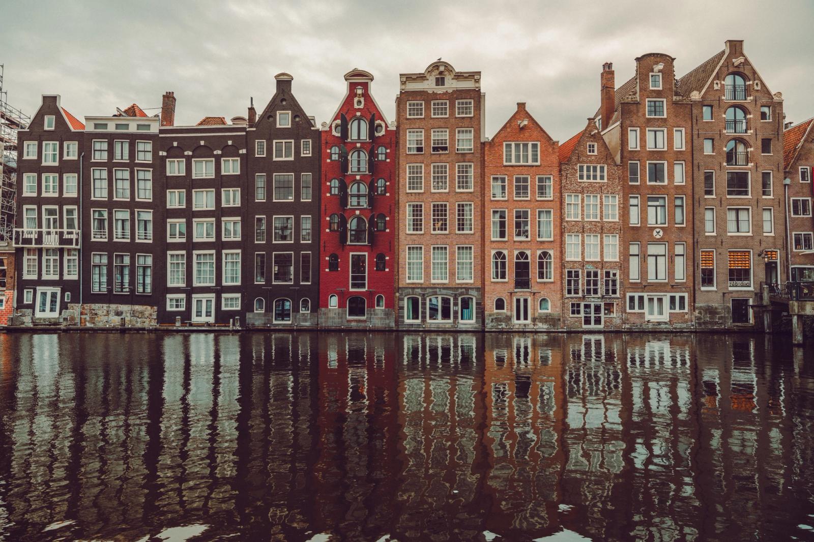 A row of tall gabled canal houses reflected in still water