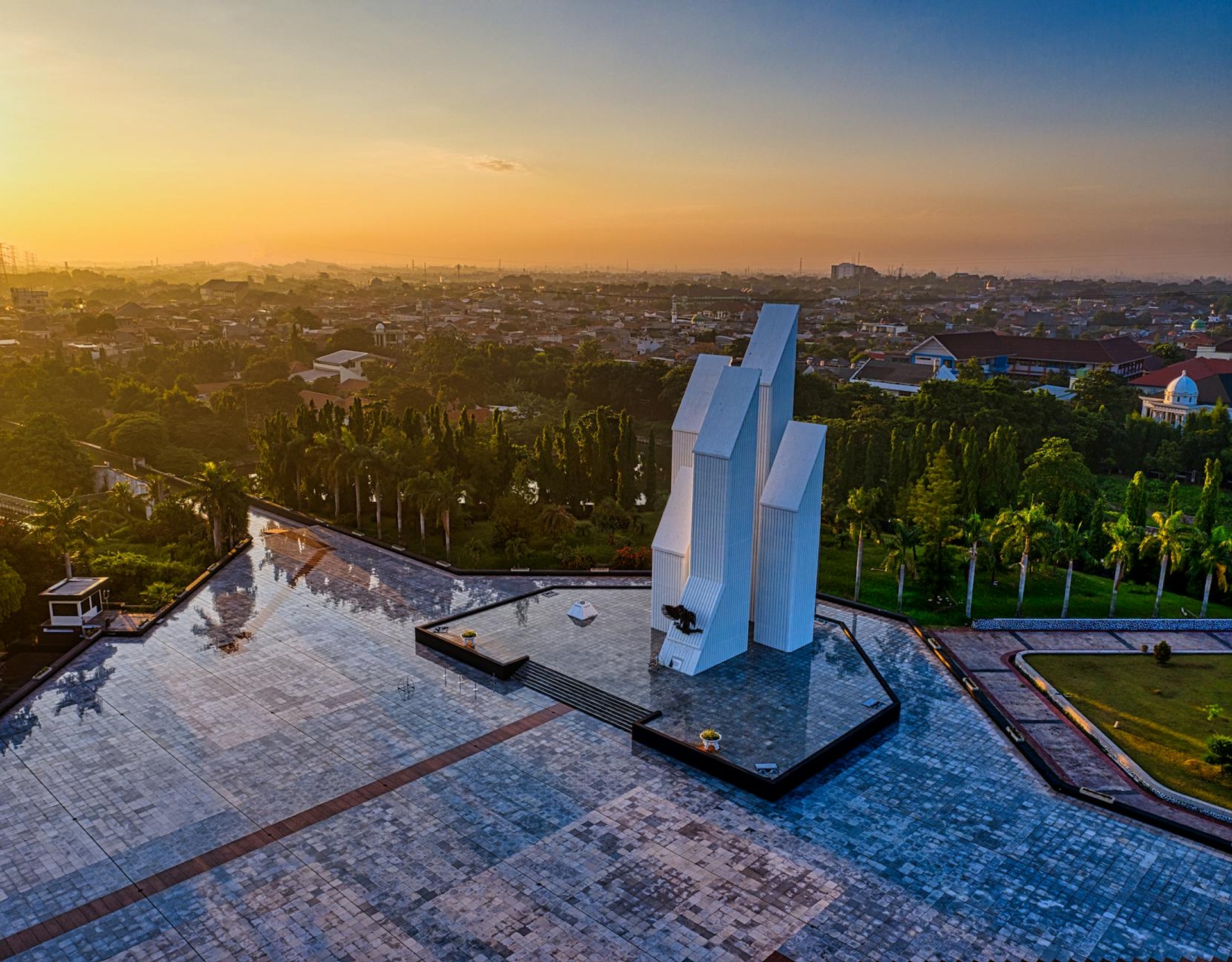 Drone view of contemporary building located on paved square in national main heroes cemetery among green trees in Indonesia at sunset time
