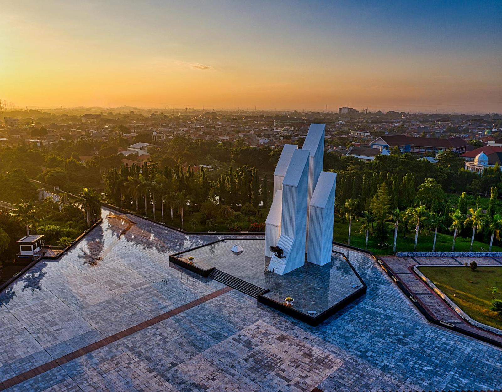 Drone view of contemporary building located on paved square in national main heroes cemetery among green trees in Indonesia at sunset time