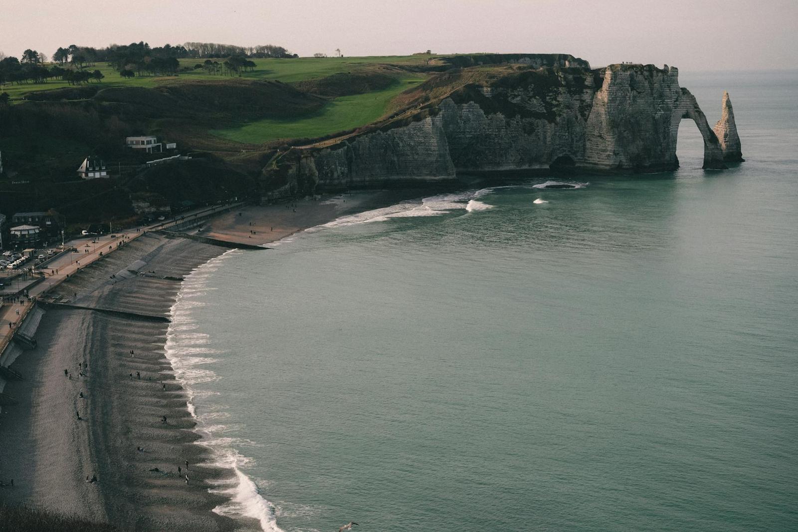 A natural rock arch jutting into the sea below green clifftop fields
