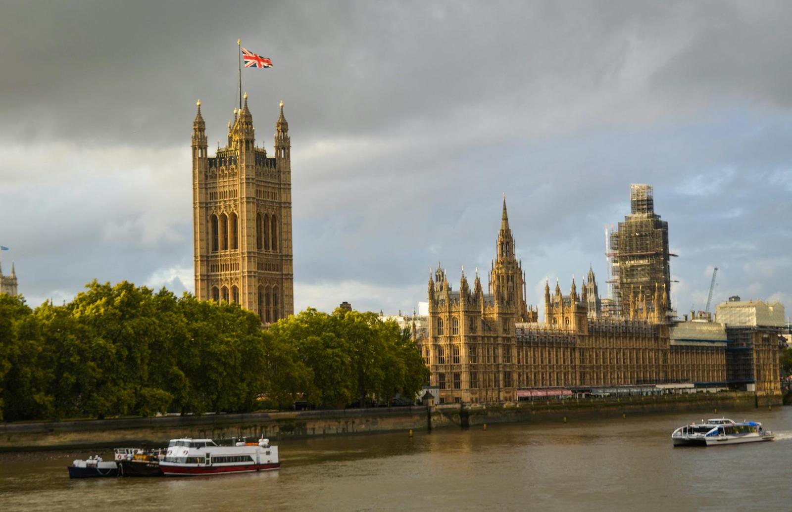 Exterior of the Houses of Parliament near river with steamboats on cloudy foggy day