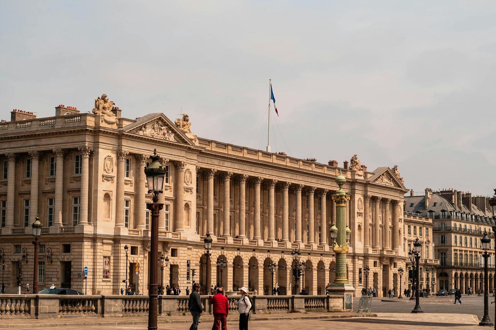 Grand colonnaded stone building facade on a city square with a flag