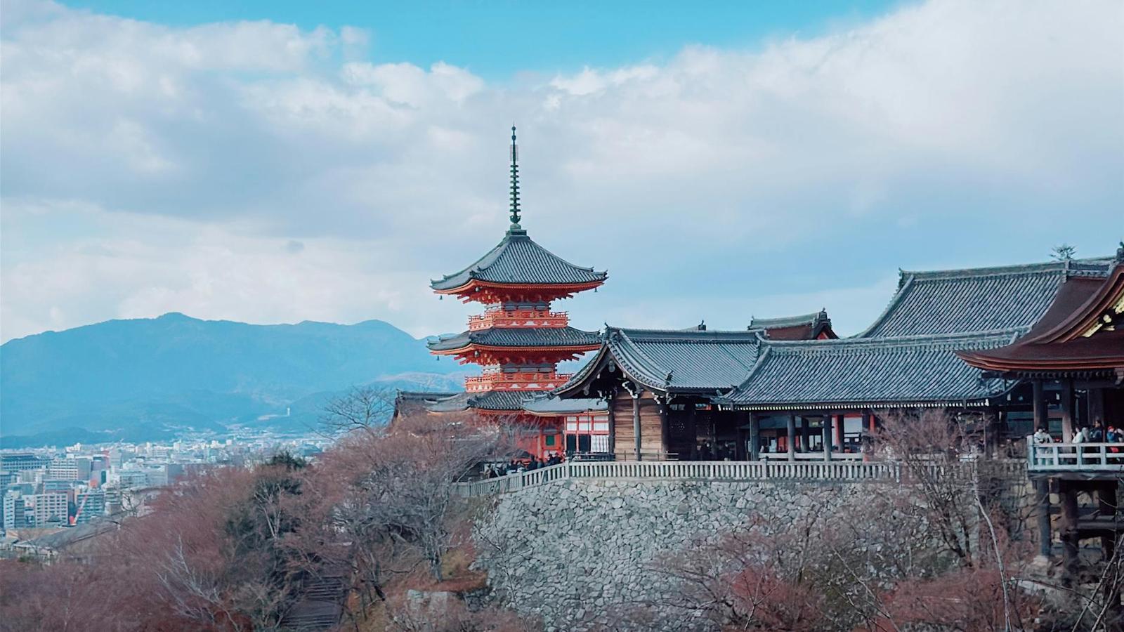 Red pagoda on a wooded hillside overlooking a distant city and mountains