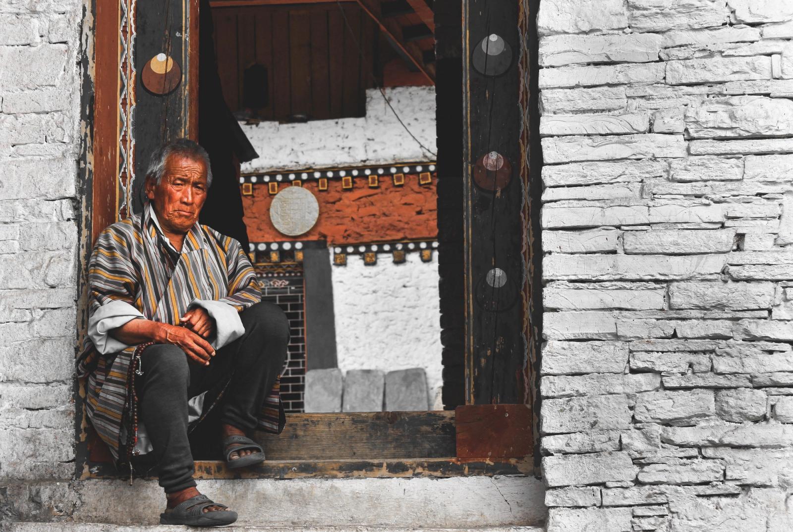 Elderly Bhutanese man in traditional attire sits in a monastery doorway, Bhutan