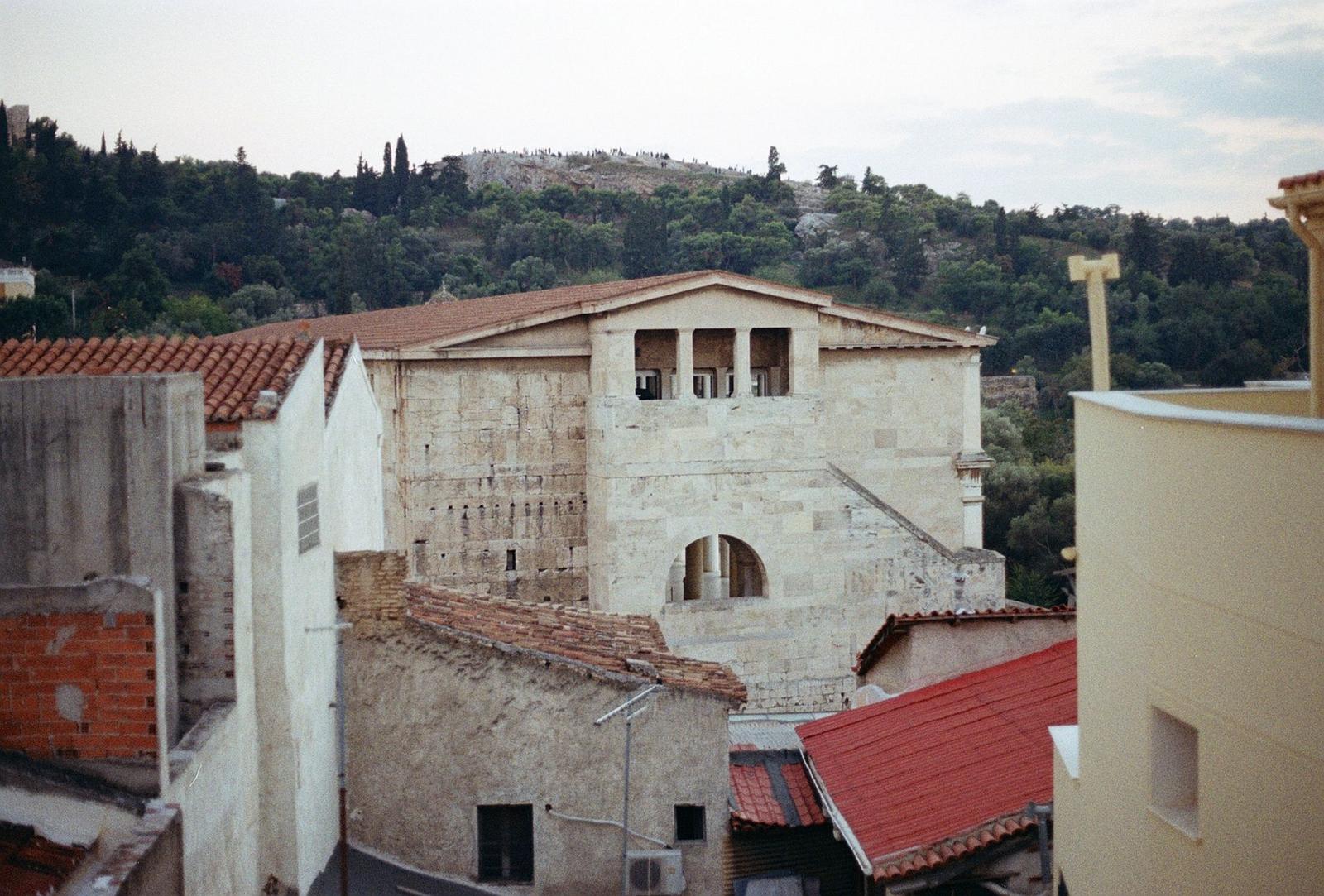 A stone building with red tile roofs set against a wooded hillside