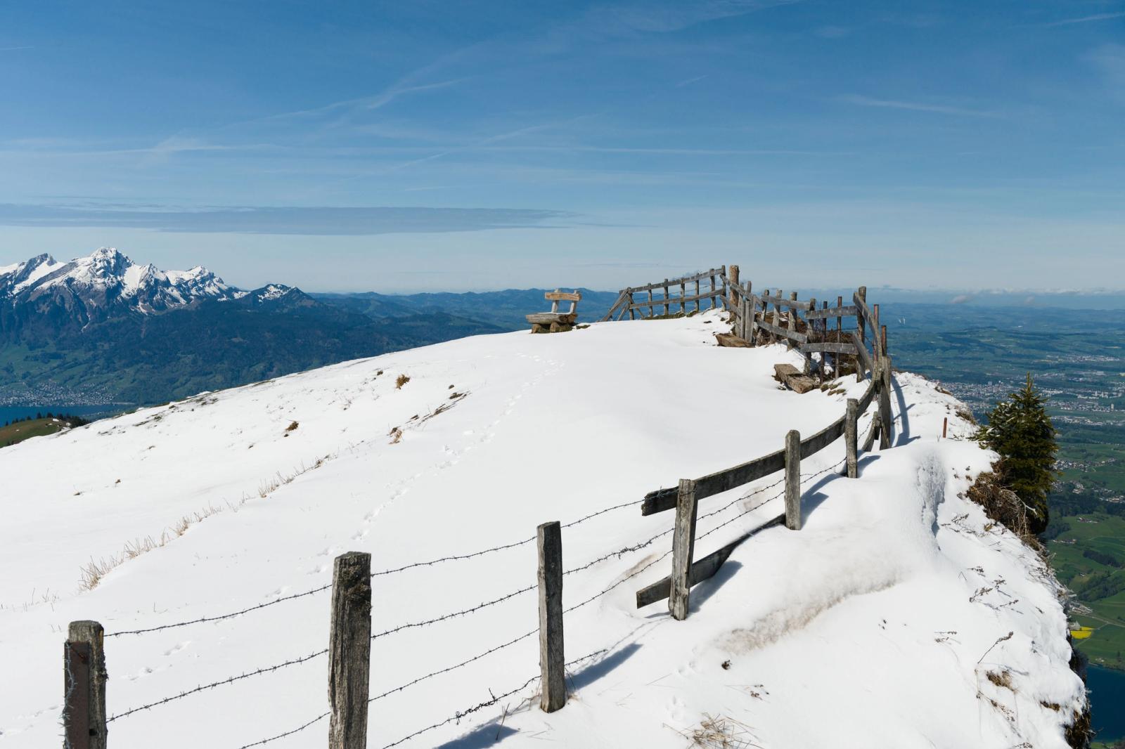 Fence and snow atop Mount Rigi with Swiss Alps in background, perfect for travel inspiration