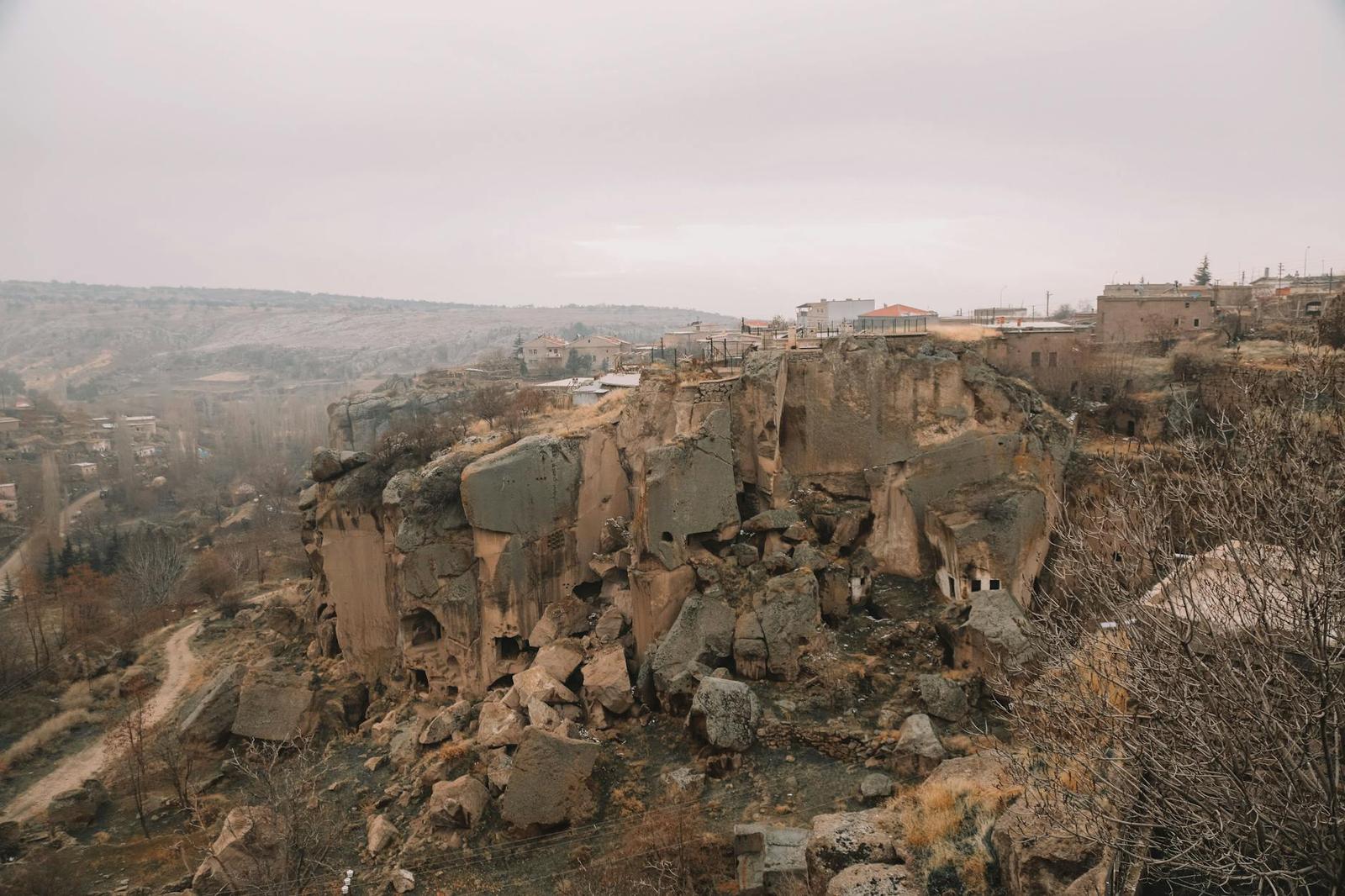 Eroded rock outcrops overlooking a hillside village under grey sky