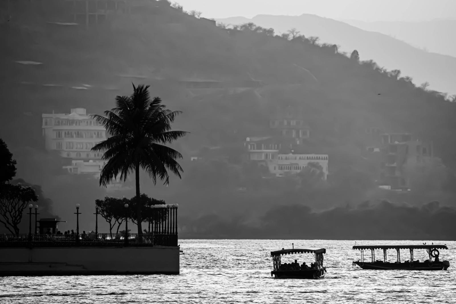 Black and white image of boats on a lake with silhouetted hills and trees, evoking tranquility