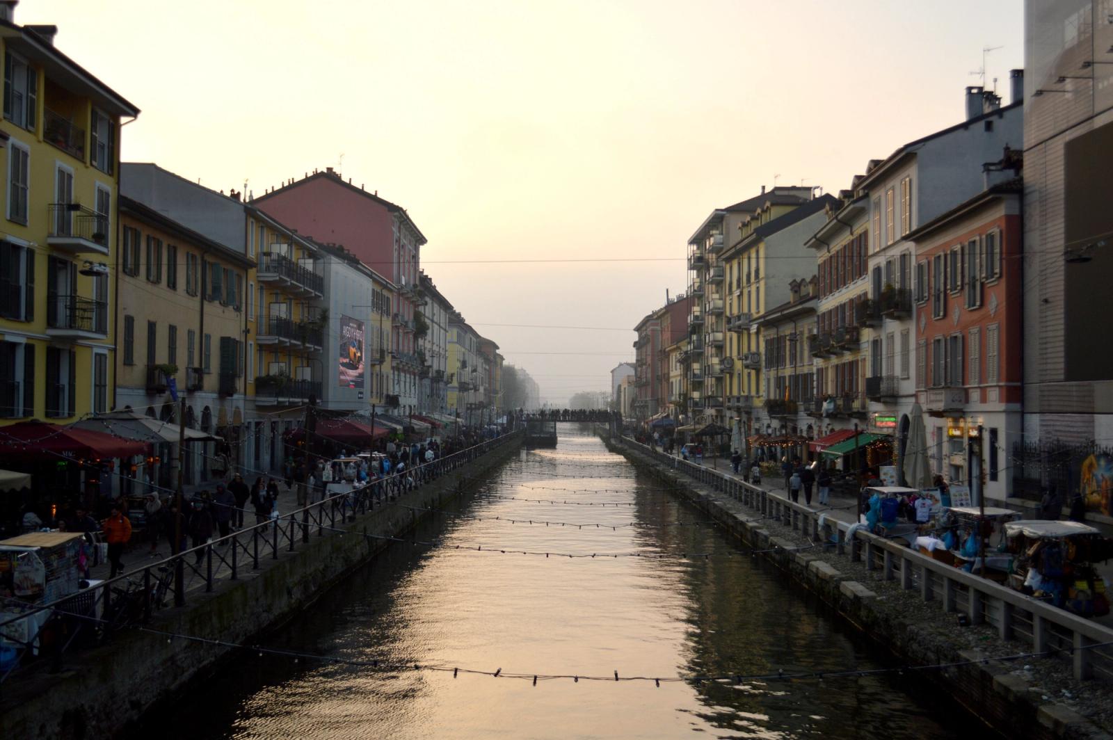 View of Naviglio Grande canal at sunset in Milan, Italy, flanked by colorful buildings and bustling streets