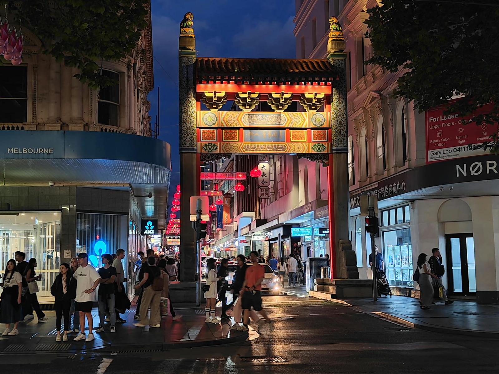 An ornate Chinatown gate glows over a busy city street at dusk
