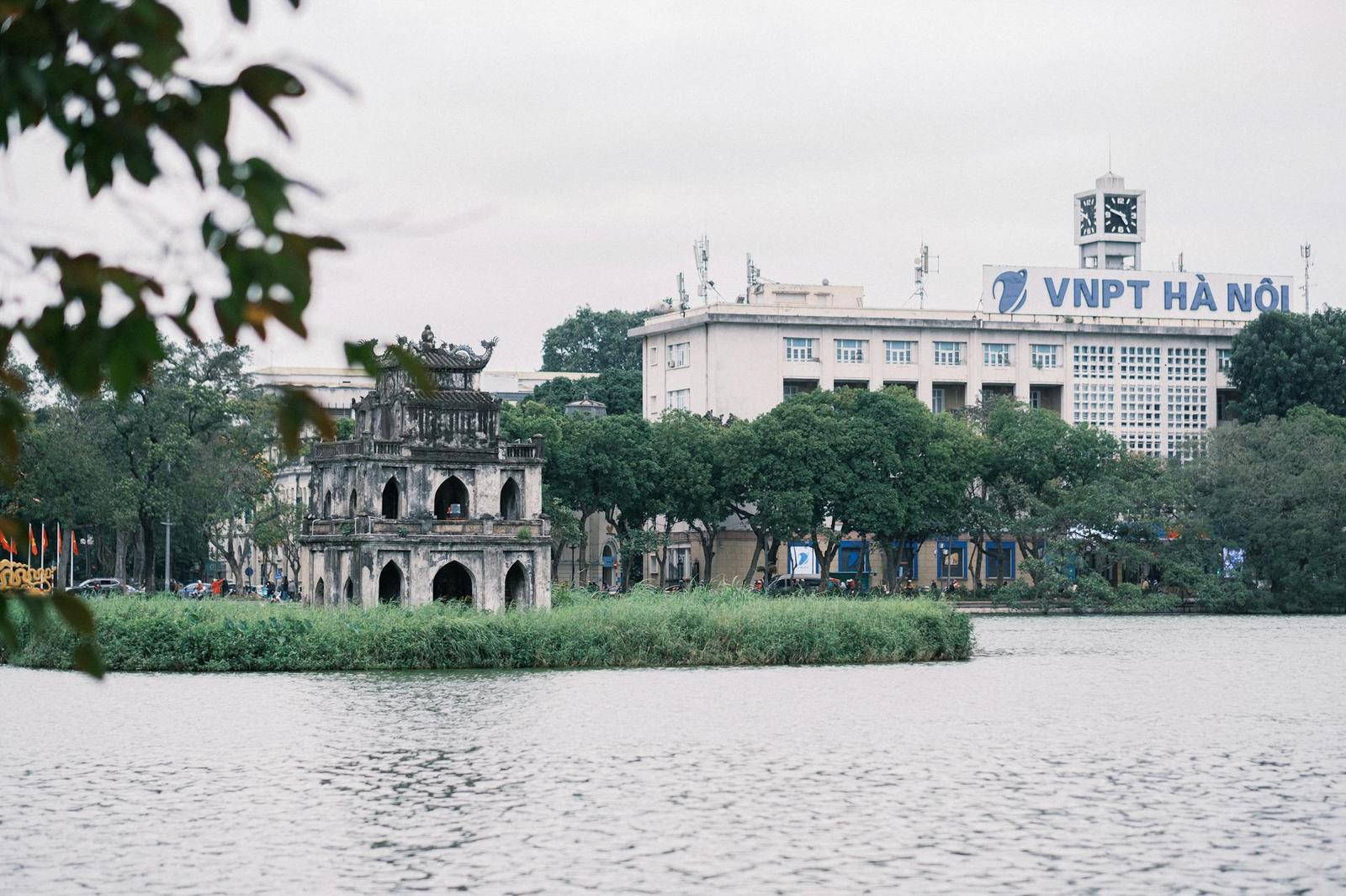 Small stone tower on a lake island with a modern building in the background