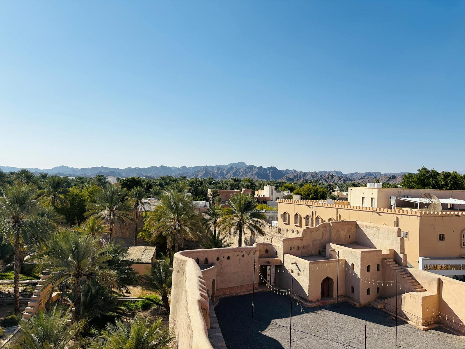 Aerial view of a sandstone fort surrounded by palm groves and mountains