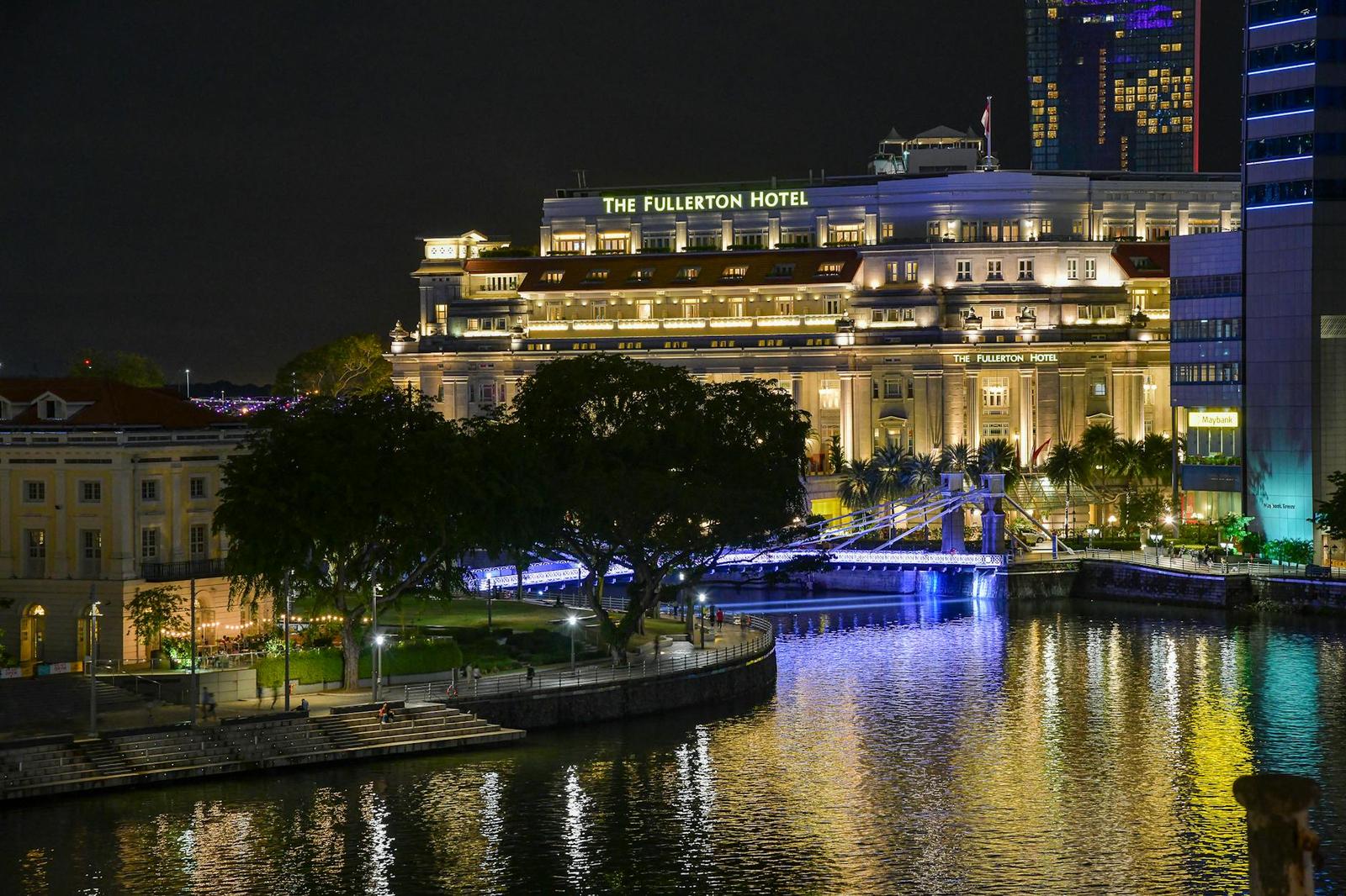 An illuminated colonial-style hotel building beside a lit garden and river at night