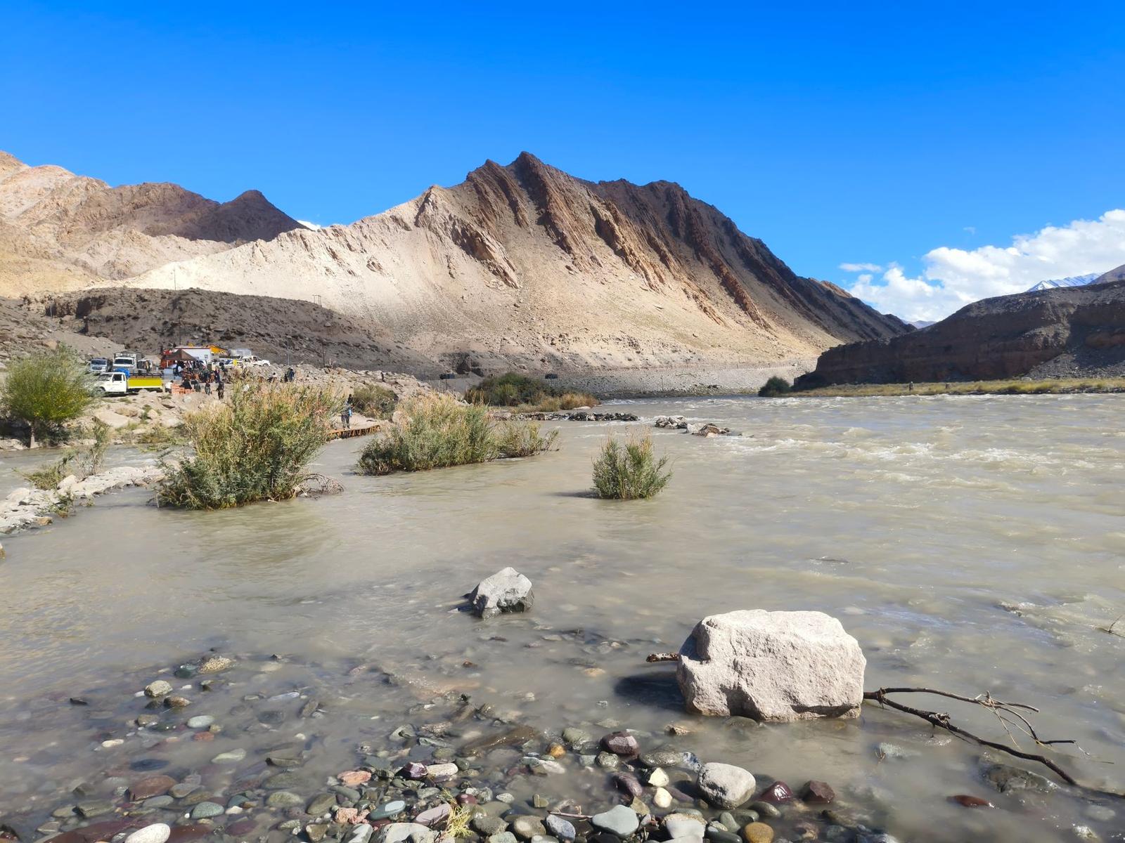 Wide glacial river flowing past rocky banks with a jeep parked near the mountains
