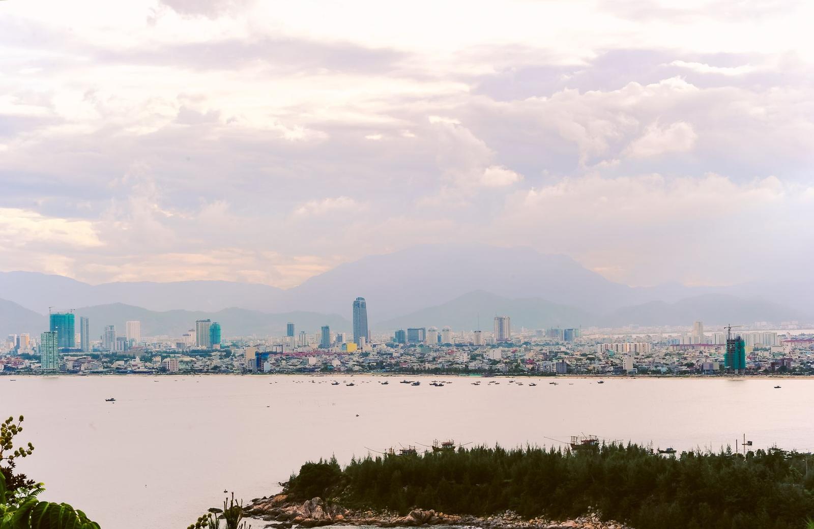 Hazy city skyline seen across a wide river with a green foreshore