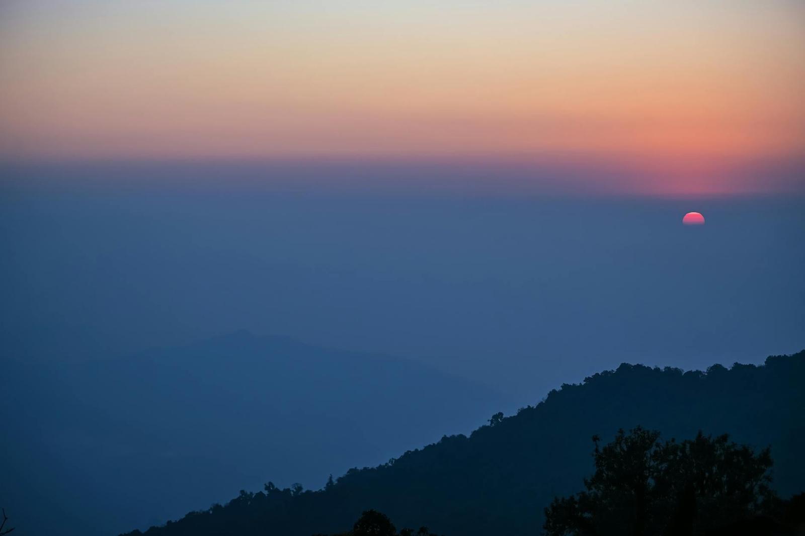 Layered mountain silhouettes glowing under a hazy sunset