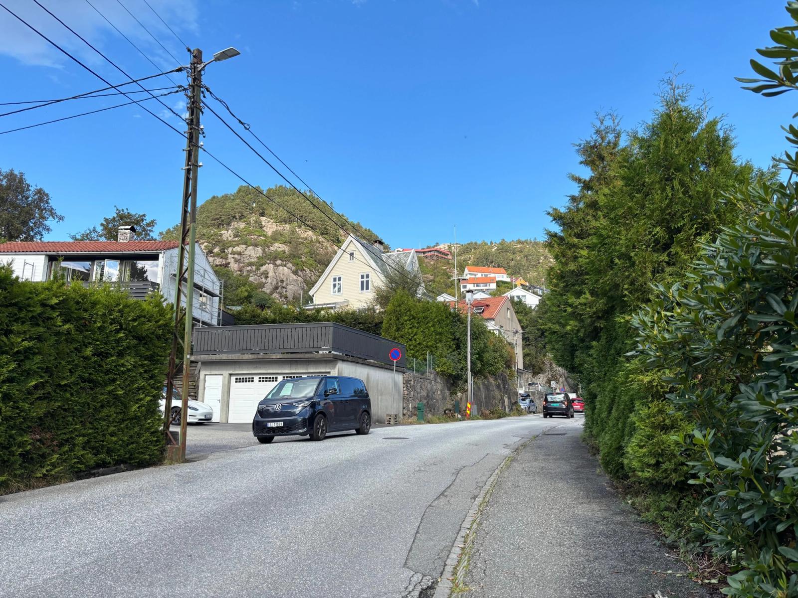 A serene street view in a hilly village in Norway, lined with houses and lush greenery under a bright blue sky