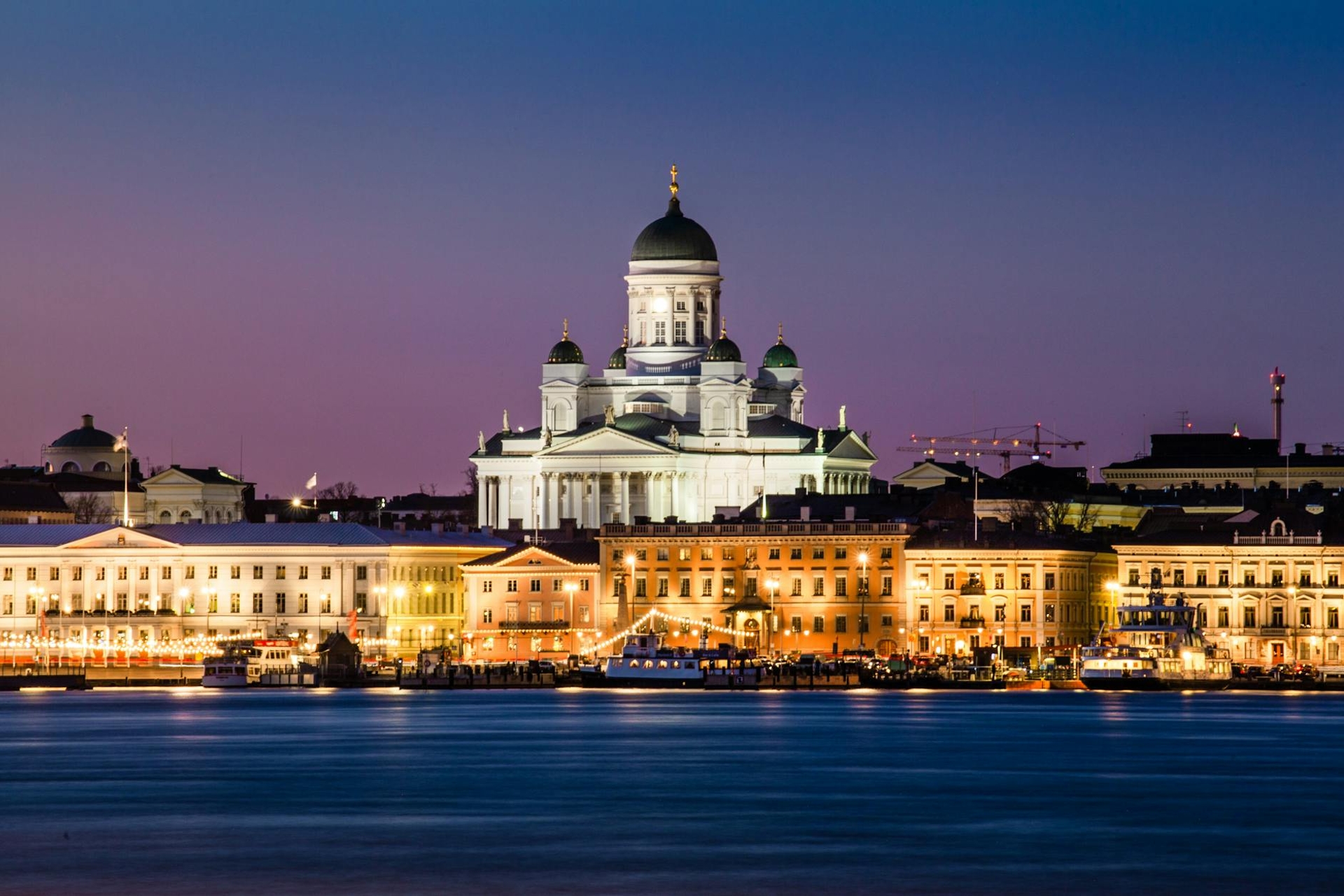 White domed cathedral lit up above a harbourfront skyline at dusk