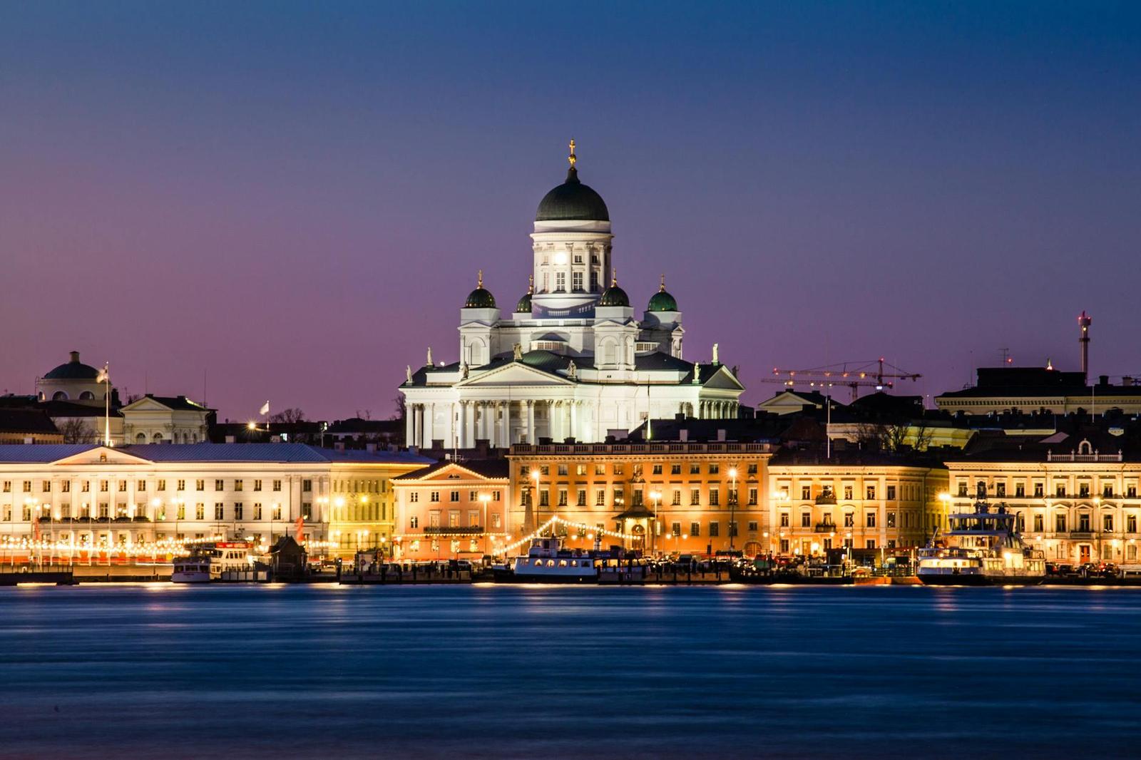 White domed cathedral lit up above a harbourfront skyline at dusk