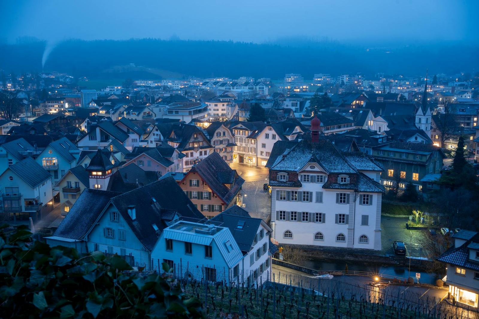 A hillside town of gabled houses glowing at dusk under a blue sky