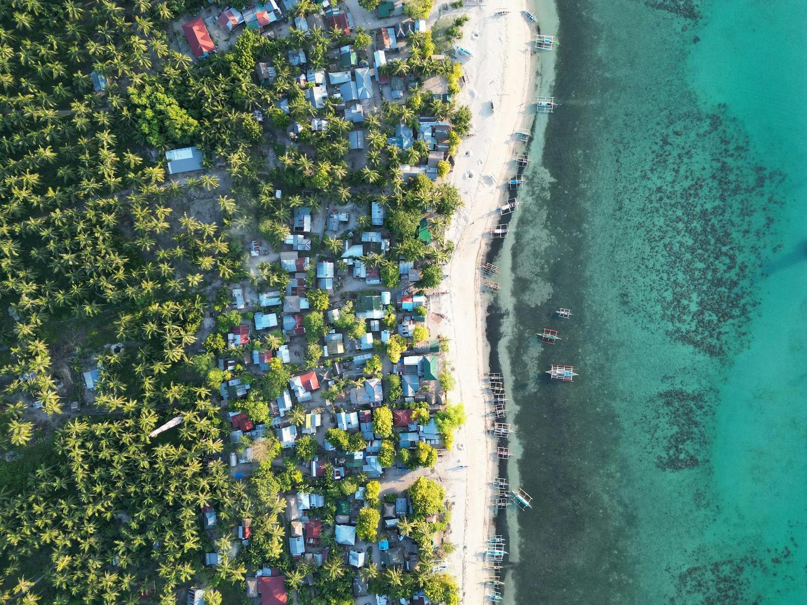 Aerial view of a dense coastal village between palms and a coral reef