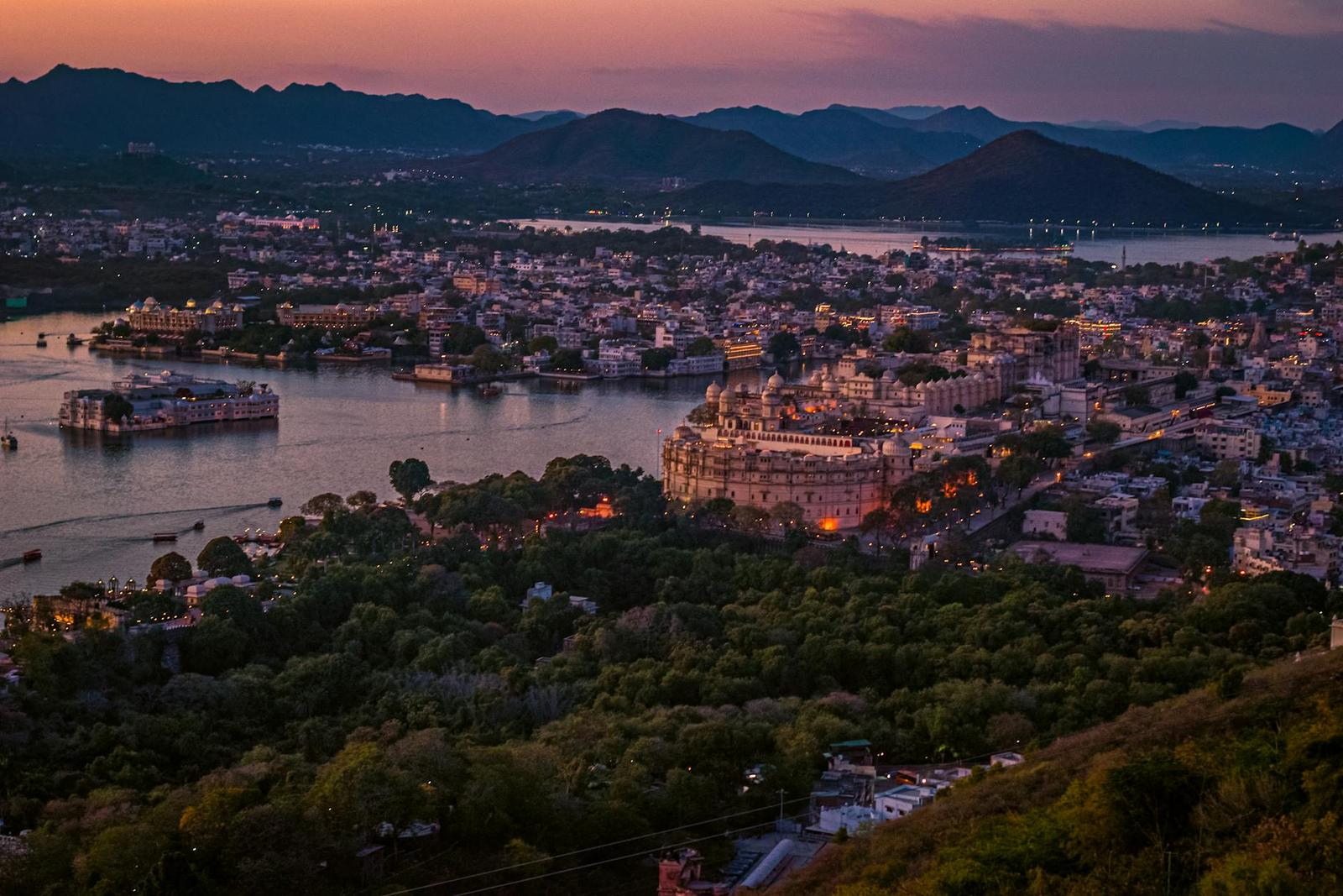A lakeside city glowing at dusk beneath distant mountains