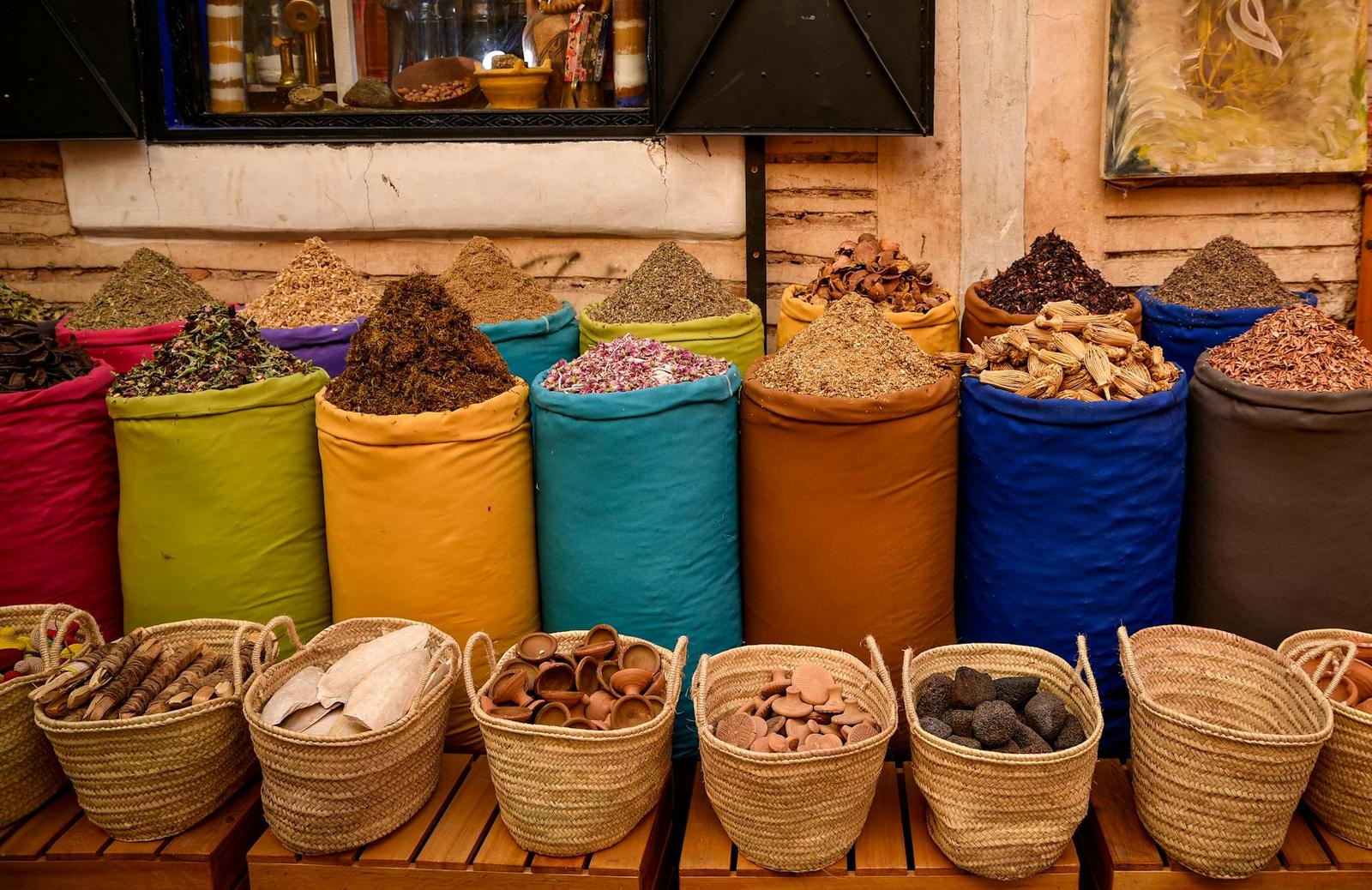 Sacks of colourful ground spices lined up beside woven market baskets